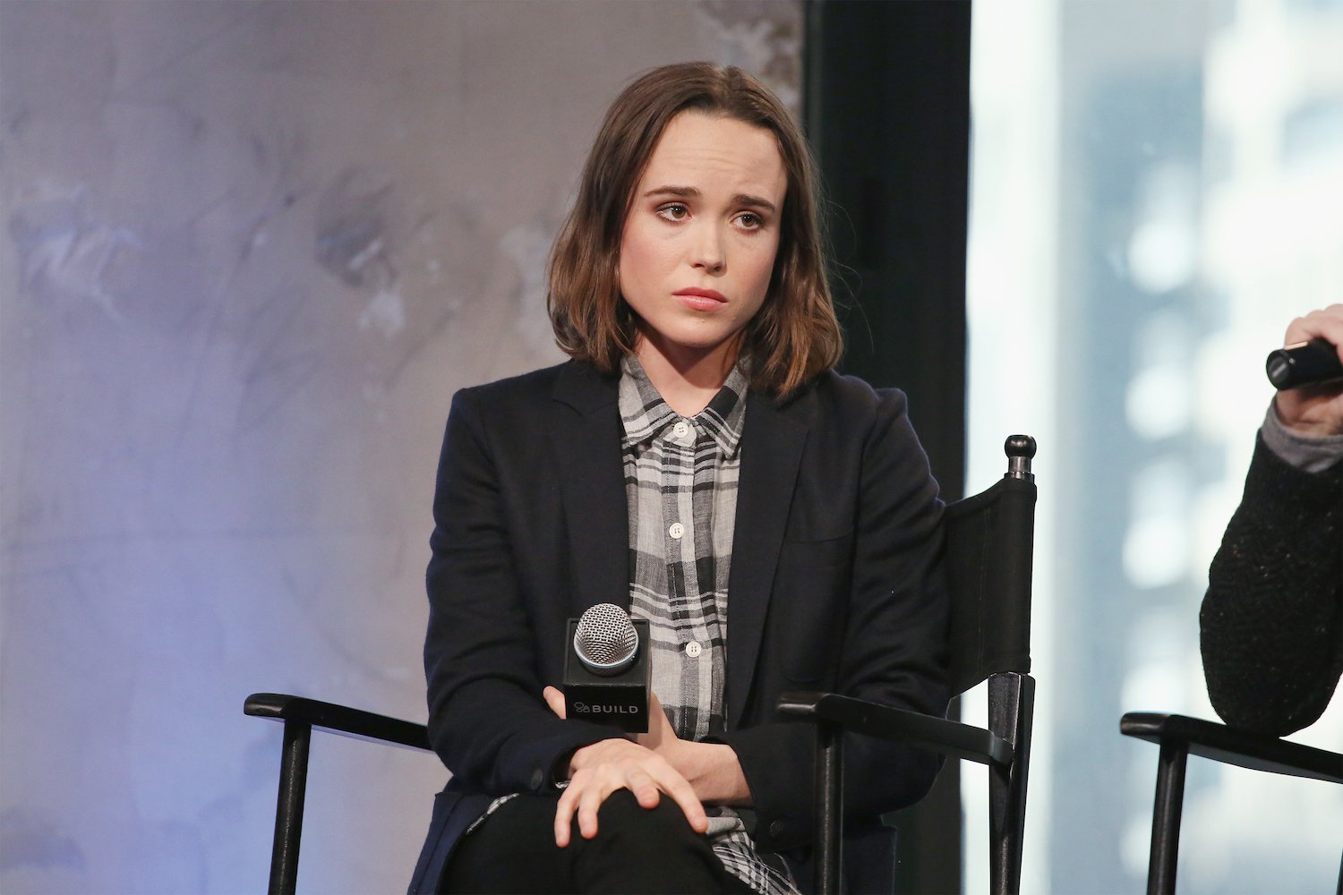 Ellen Page not smiling, looking away from the camera holding a microphone