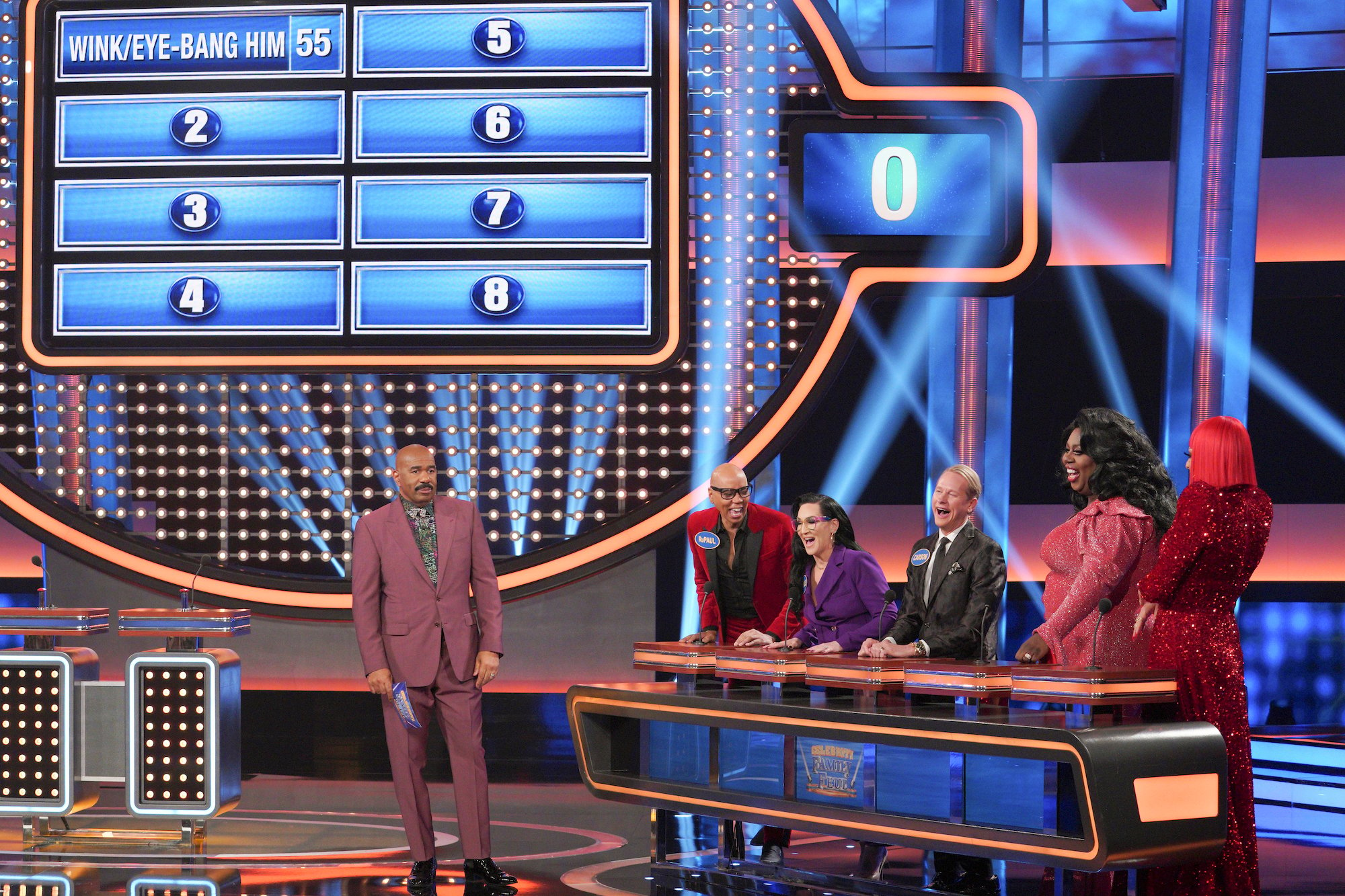 Steve Harvey in front of a Family Feud board next to the cast of RuPauls Drag Race