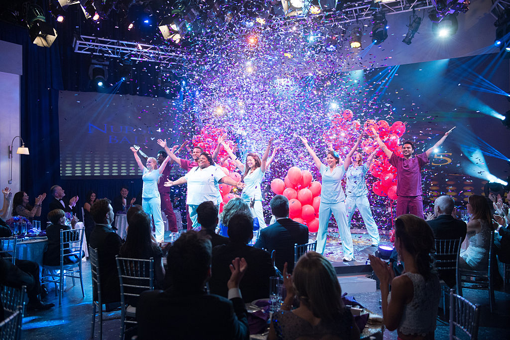 Cast dressed as nurses on stage doing a dance routine while balloons and confetti fall from the ceiling