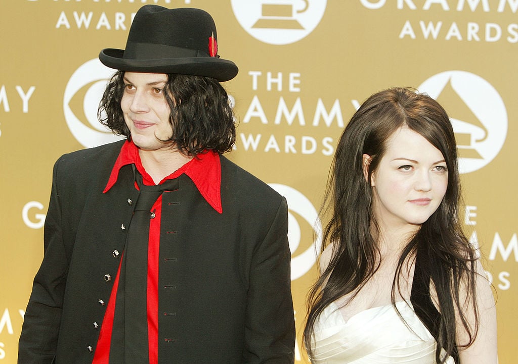 Jack White and Meg White smiling in front of a beige background with a repeating logo