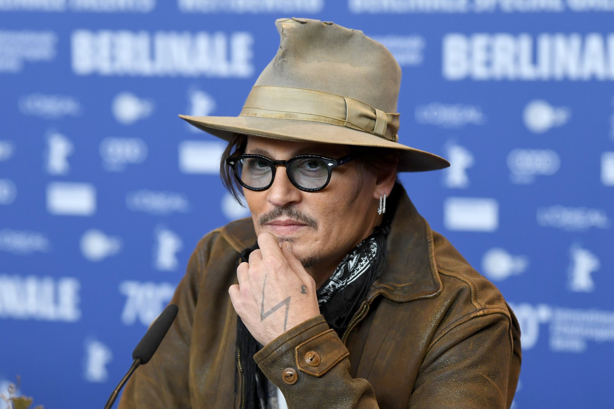 Johnny Depp in a hat and glasses in front of a blurred blue background