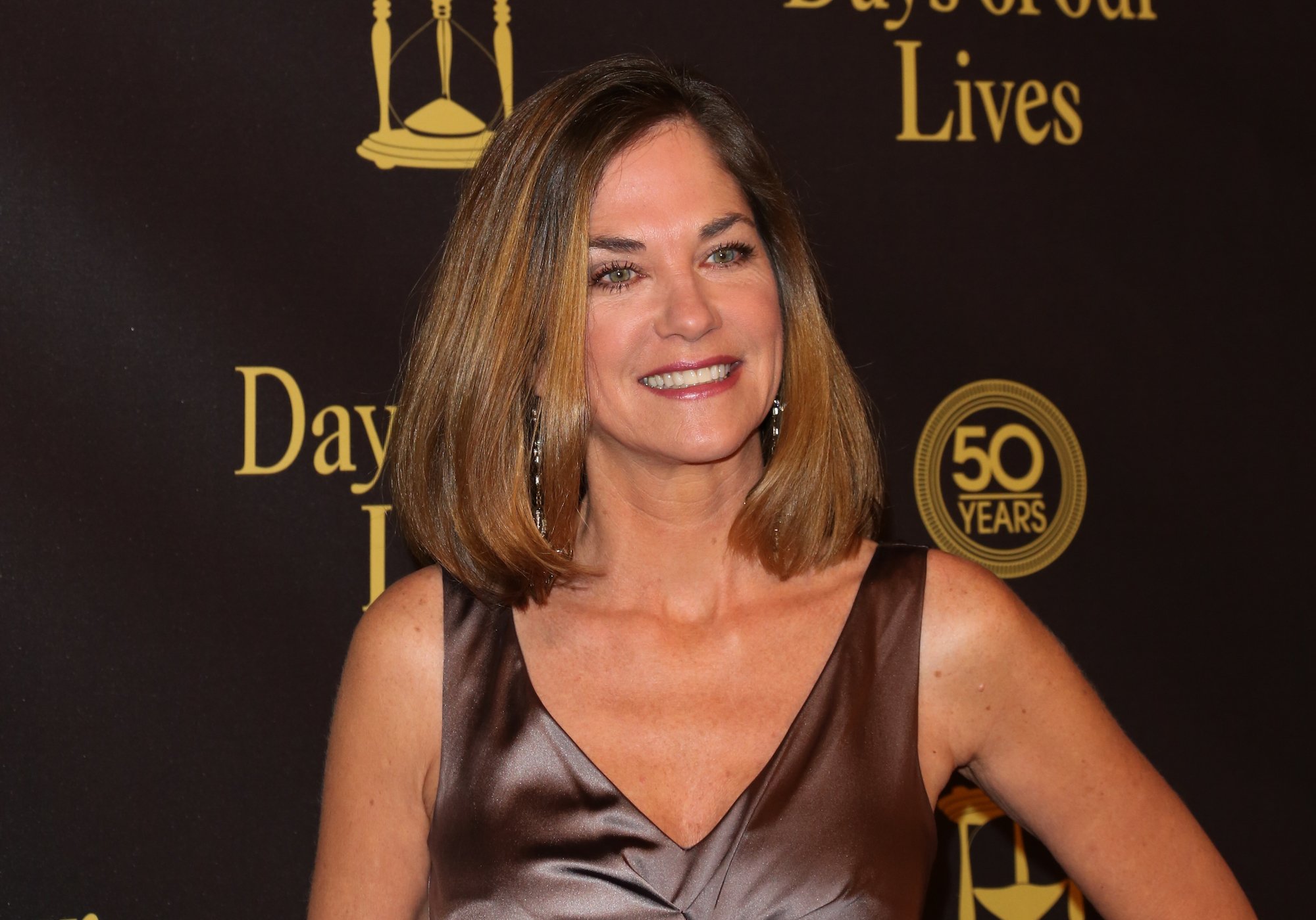 Kassie Depaiva smiling in front of a brown backdrop with the 'Days of our Lives' logo