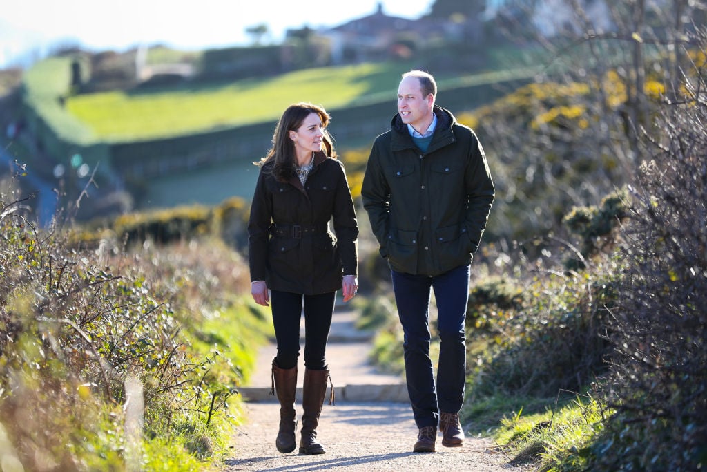 Kate Middleton and Prince William smiling, walking a dirt path surrounded by fields
