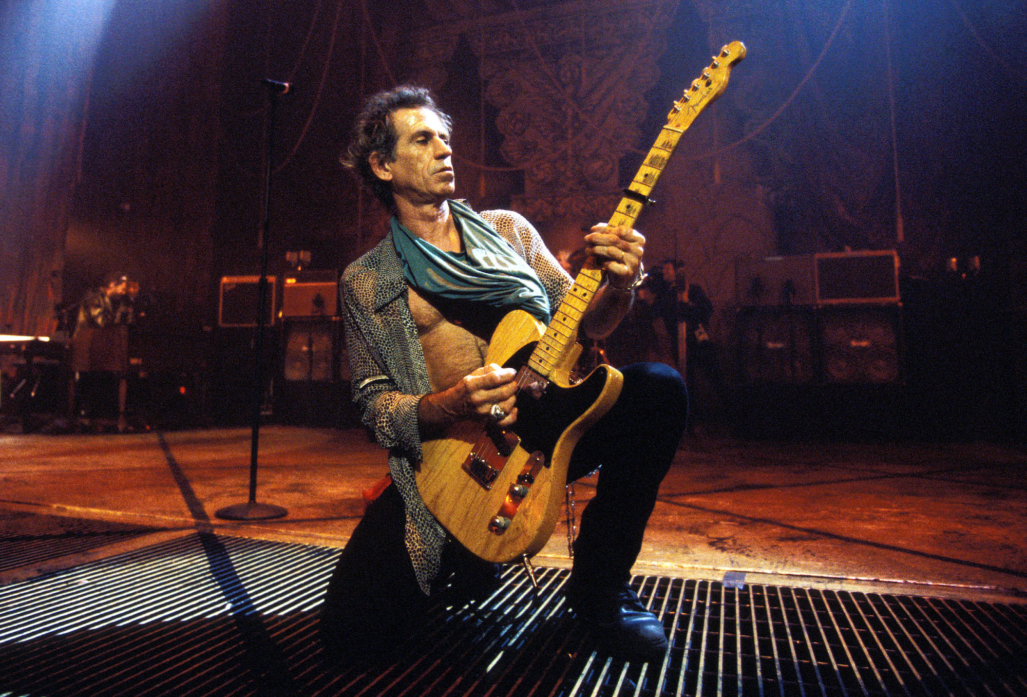 Keith Richards kneeling on stage holding a guitar, looking to the right