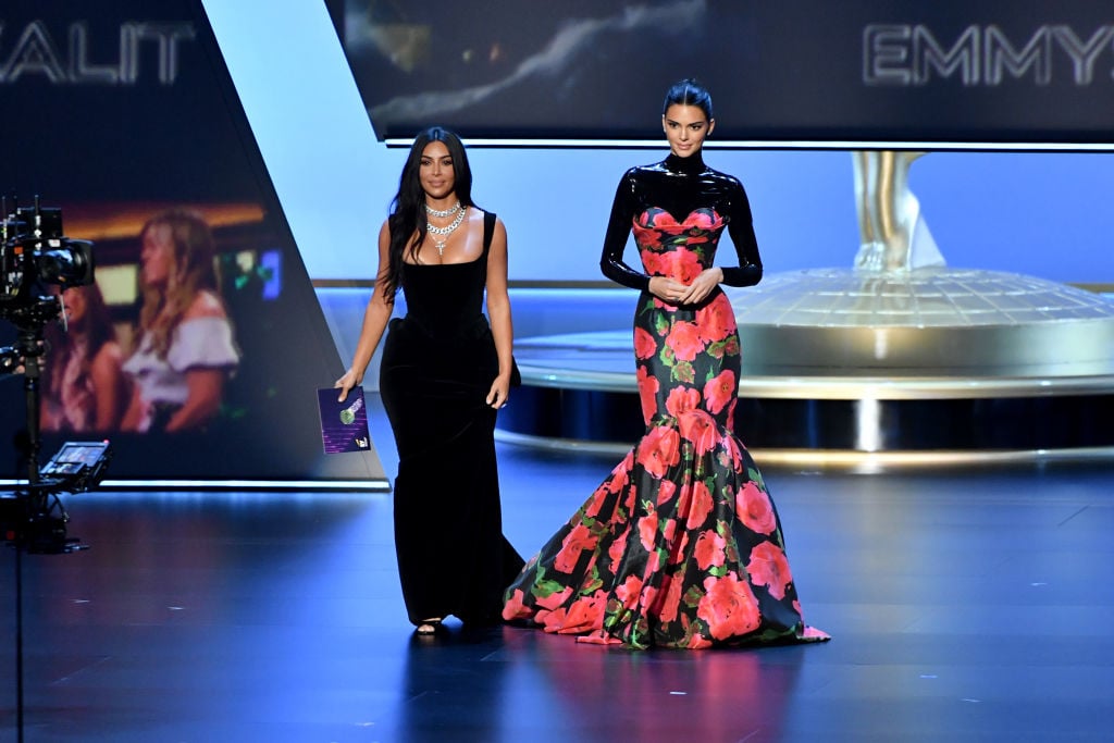 Kim Kardashian and Kendall Jenner smiling, walking on a stage