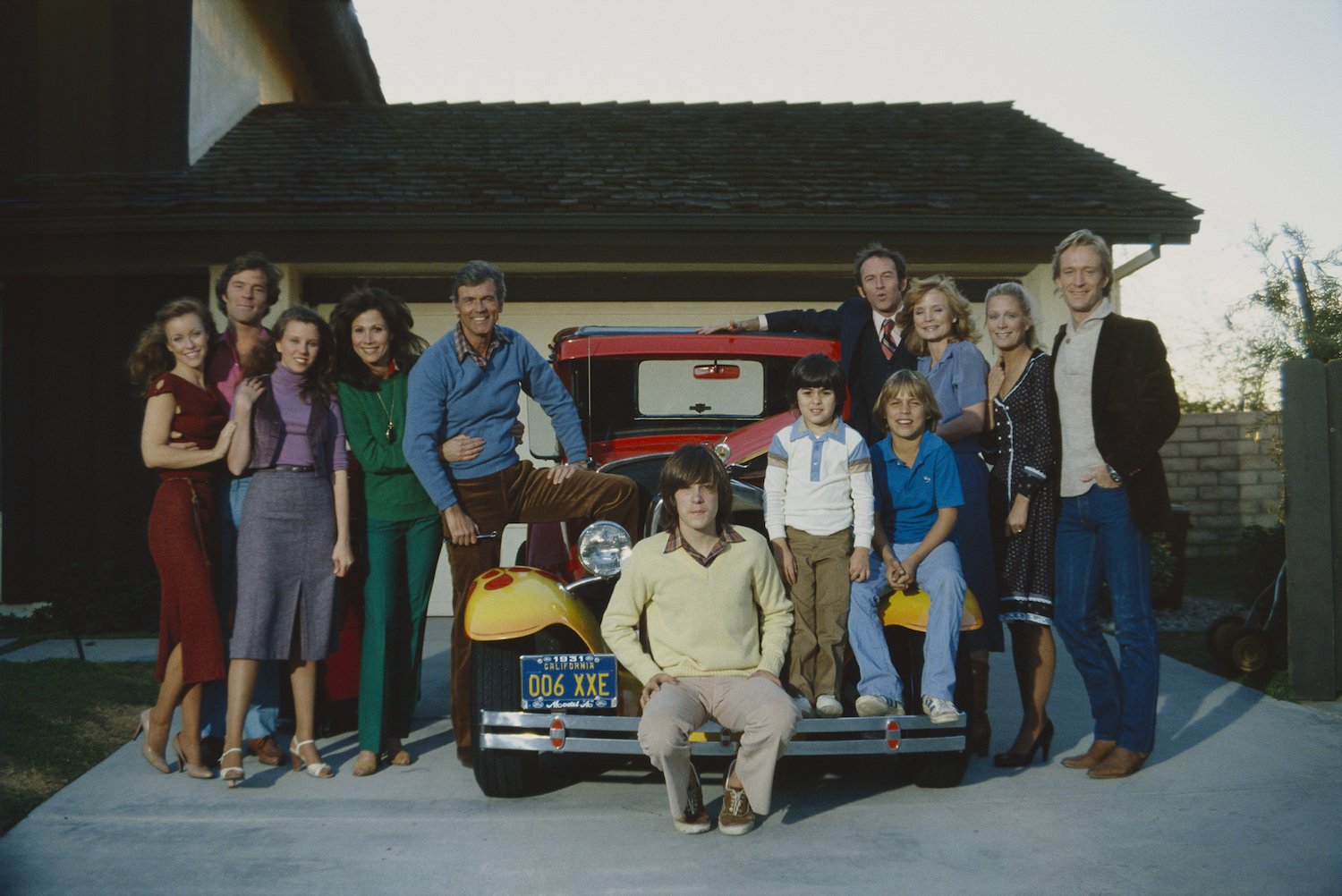 Knots Landing cast surrounding a car parked in a driveway smiling at the camera