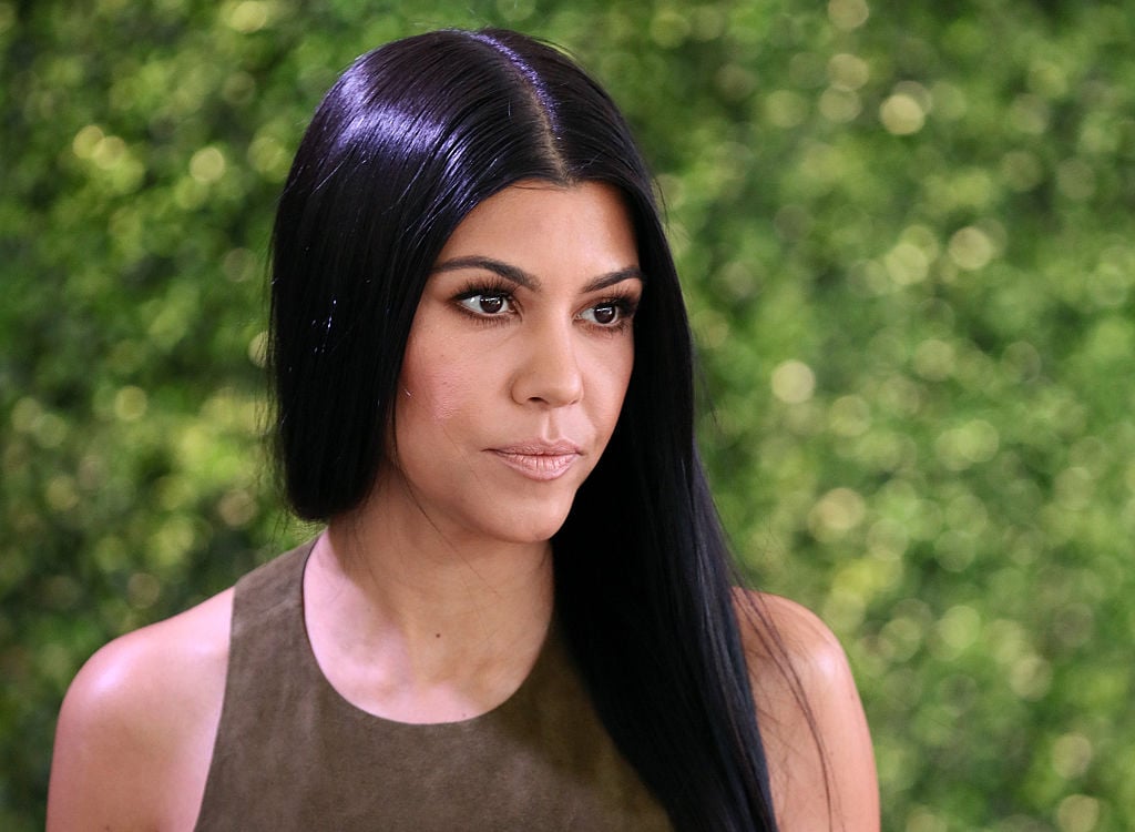 Kourtney Kardashian looking off to the side in front of a blurred green background