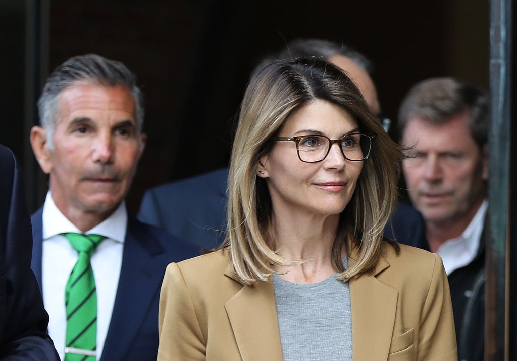 Lori Loughlin smiling wearing a blazer, walking out of a courthouse