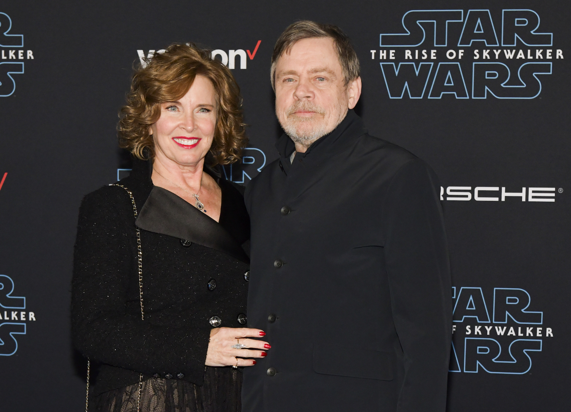 Marilou York and Mark Hamill smilng in front of a dark background with a repeating Star Wars logo