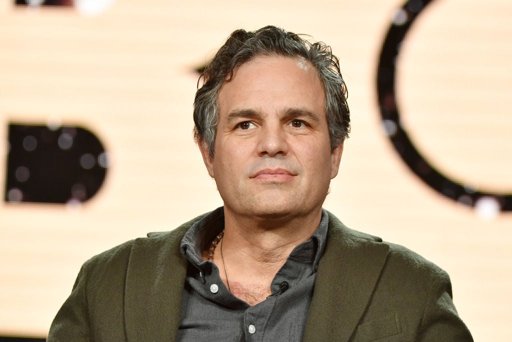 Mark Ruffalo looking off camera, not smiling, sitting down in front of a blurred background