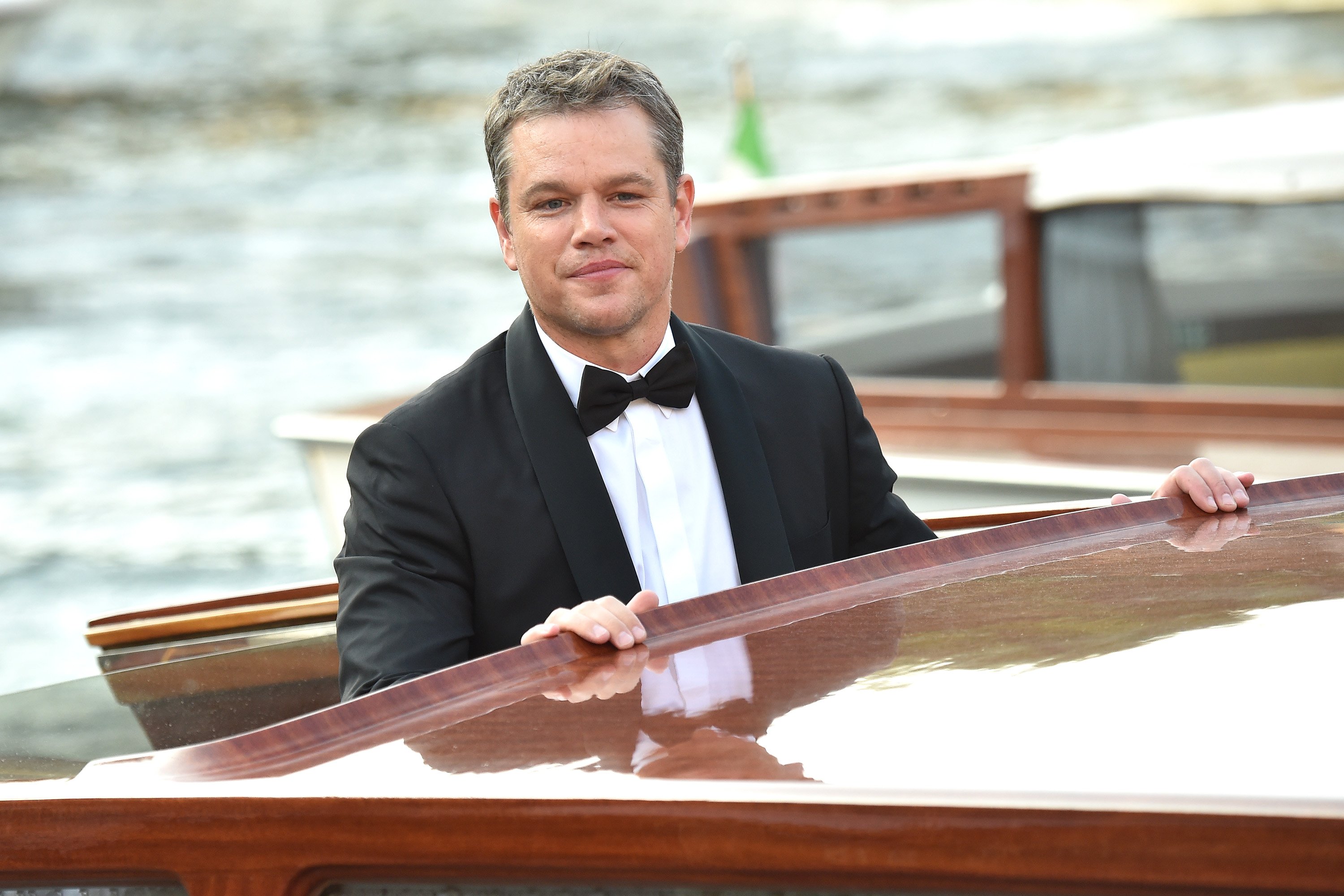 Matt Damon smiling, looking over the top of a canal bus in Venice