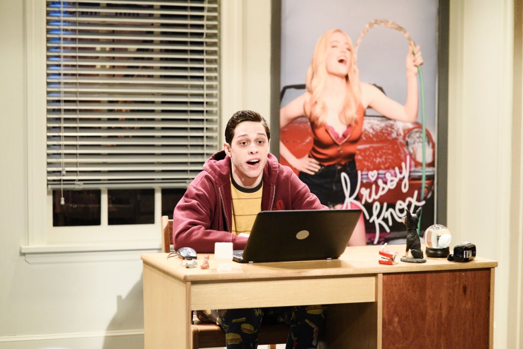Pete Davidson on set of 'Saturday Night Live' sitting at a desk