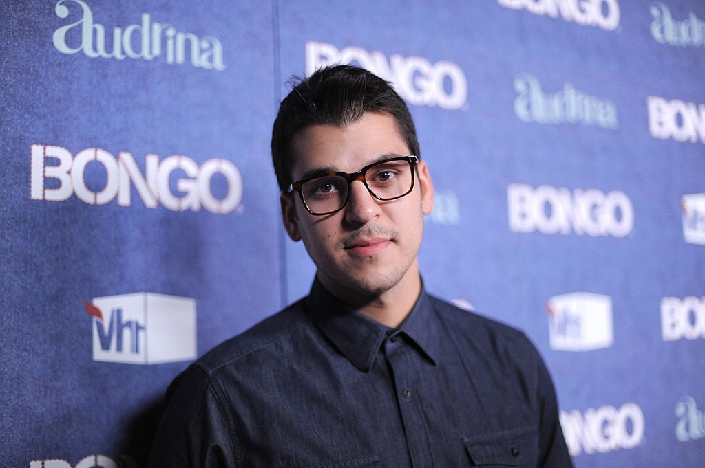 Rob Kardashian wearing glasses in front of a blue background with repeating logo