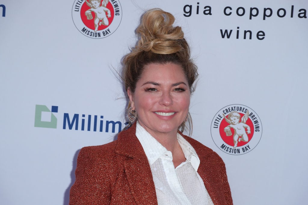 Shania Twain smiling in front of a white background with repeating logos