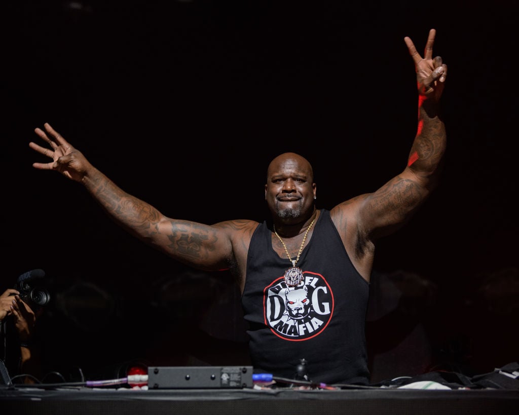 Shaquille O'Neal smiling holding up a peace sign behind a DJ set