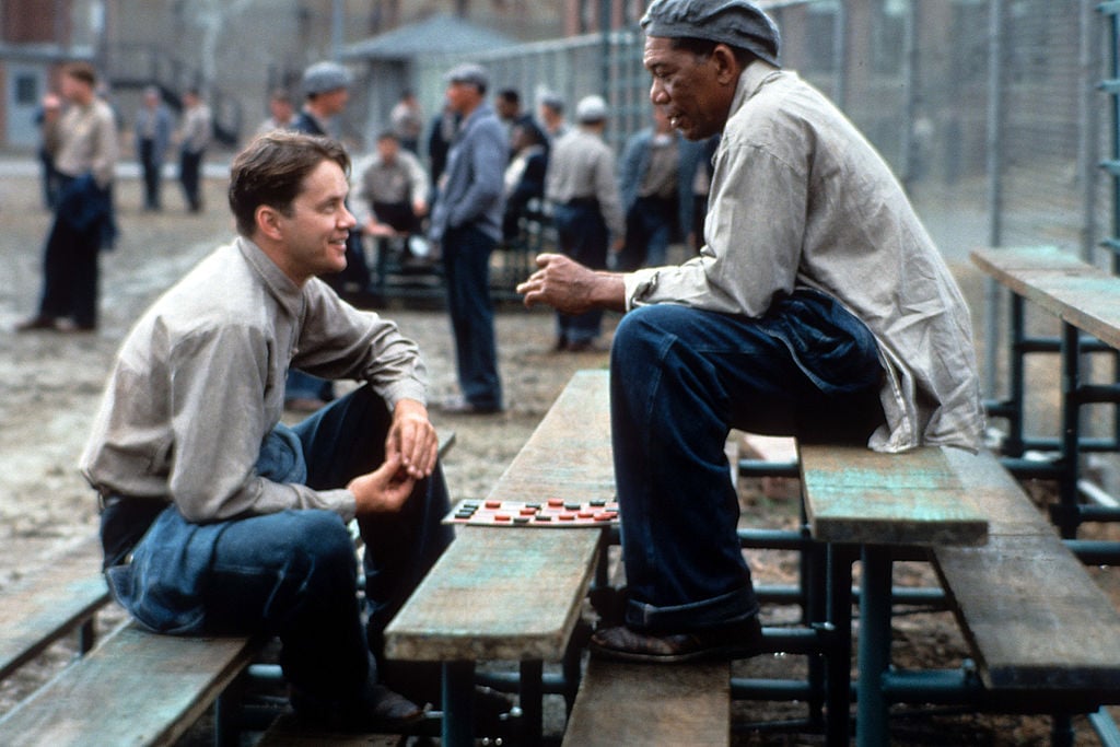 Tim Robbins and Morgan Freeman sitting outside on the benches playing checkers and talking in a scene from the film 'The Shawshank Redemption'  