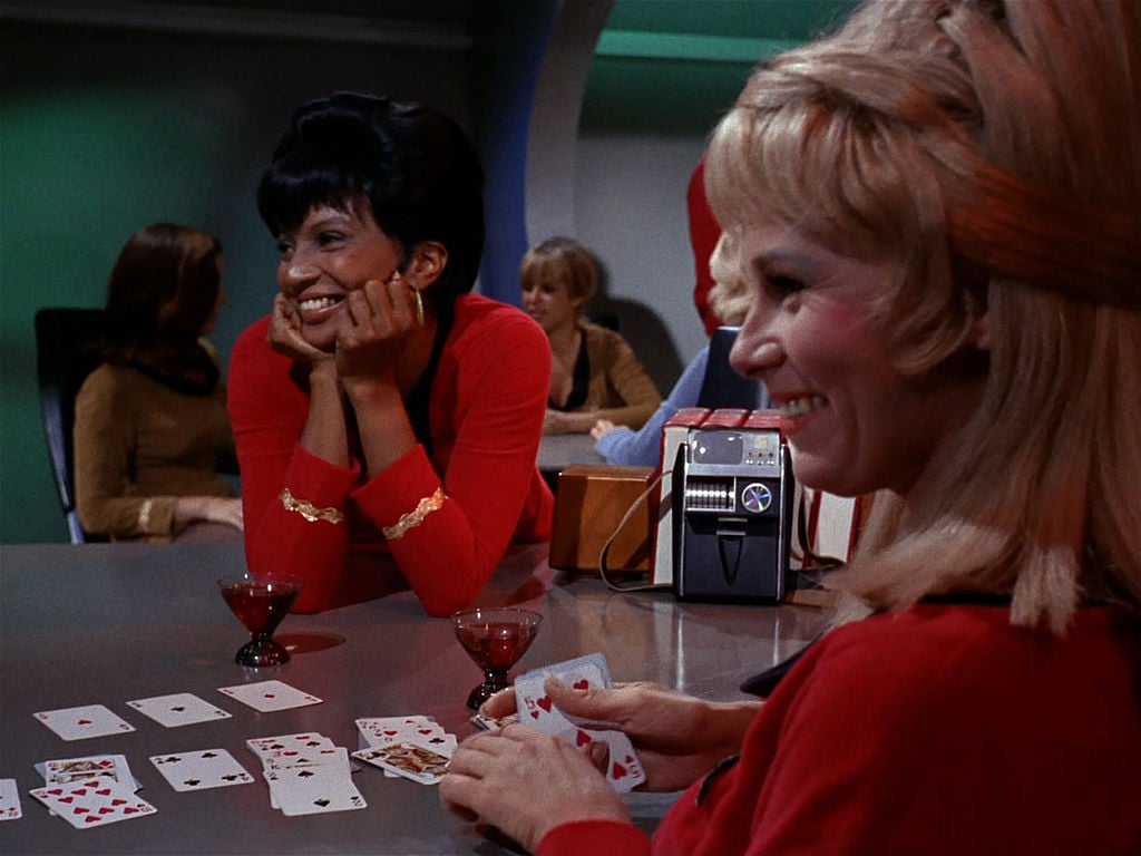 Nichelle Nichols as Lieutenant Uhura, sitting at a card table with drinks, smiling