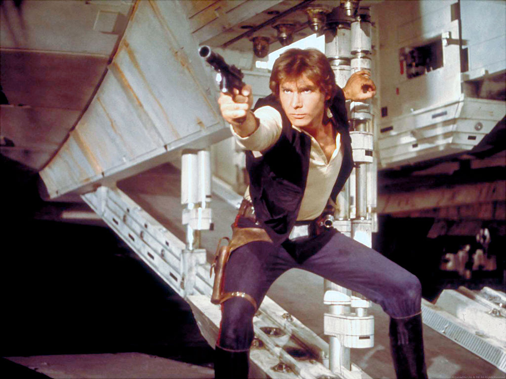 Harrison Ford as Hans Solo on set of 'Star Wars' pointing a gun to the side of the camera