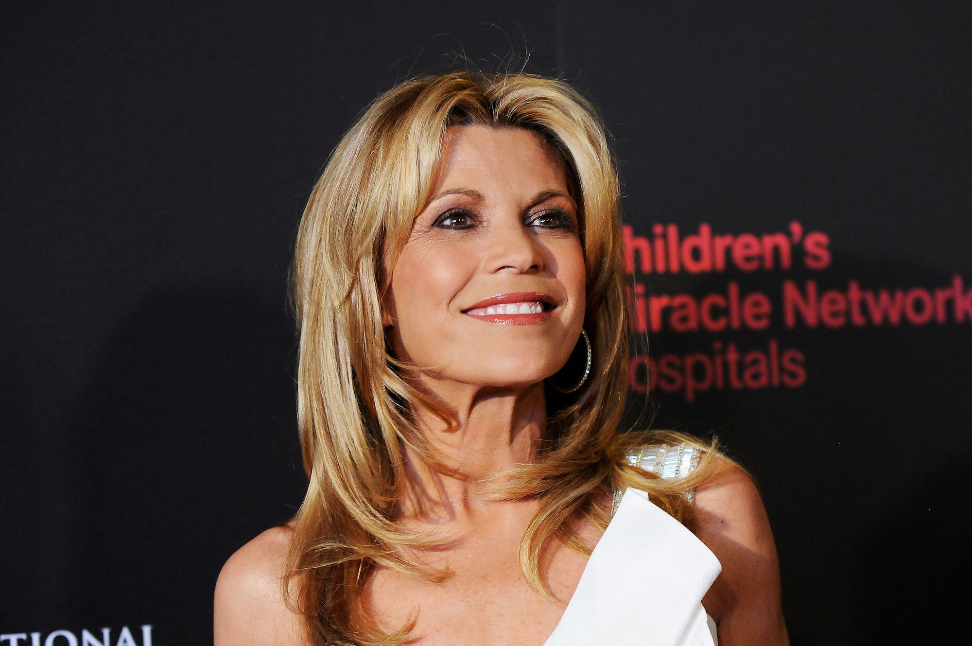 Vanna White smiling in front of a black background, looking up