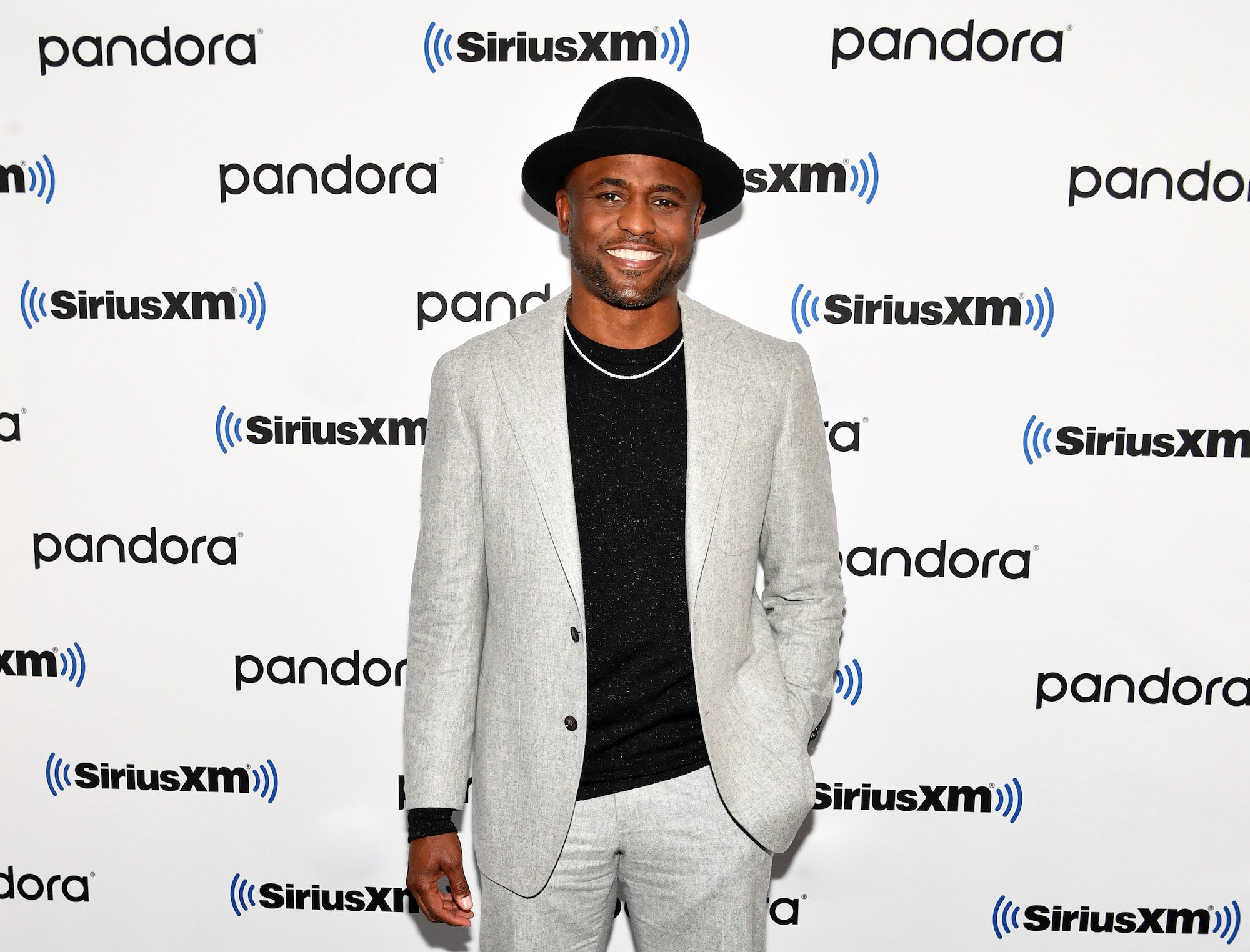Wayne Brady smiling in front of a repeating background