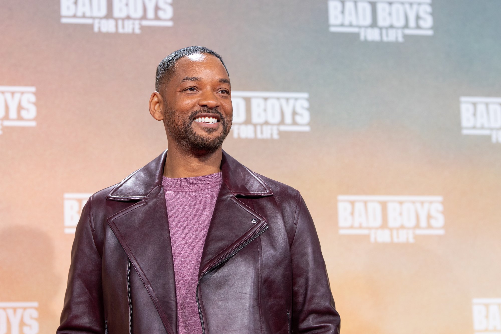 Will Smith smiling, looking away from the camera, wearing a dark red leather jacket