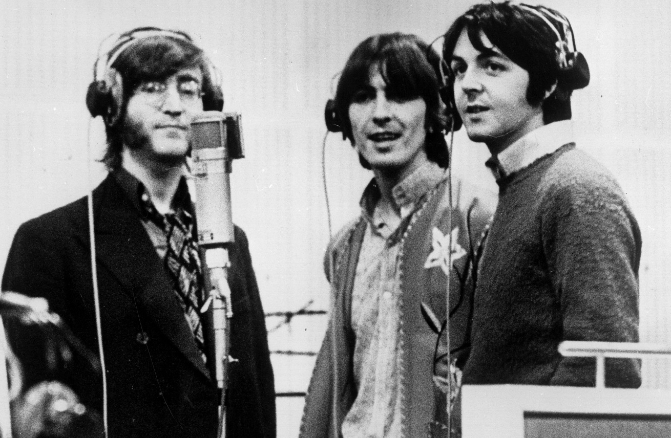 John Lennon, George Harrison. and Paul McCartney standing at a microphone