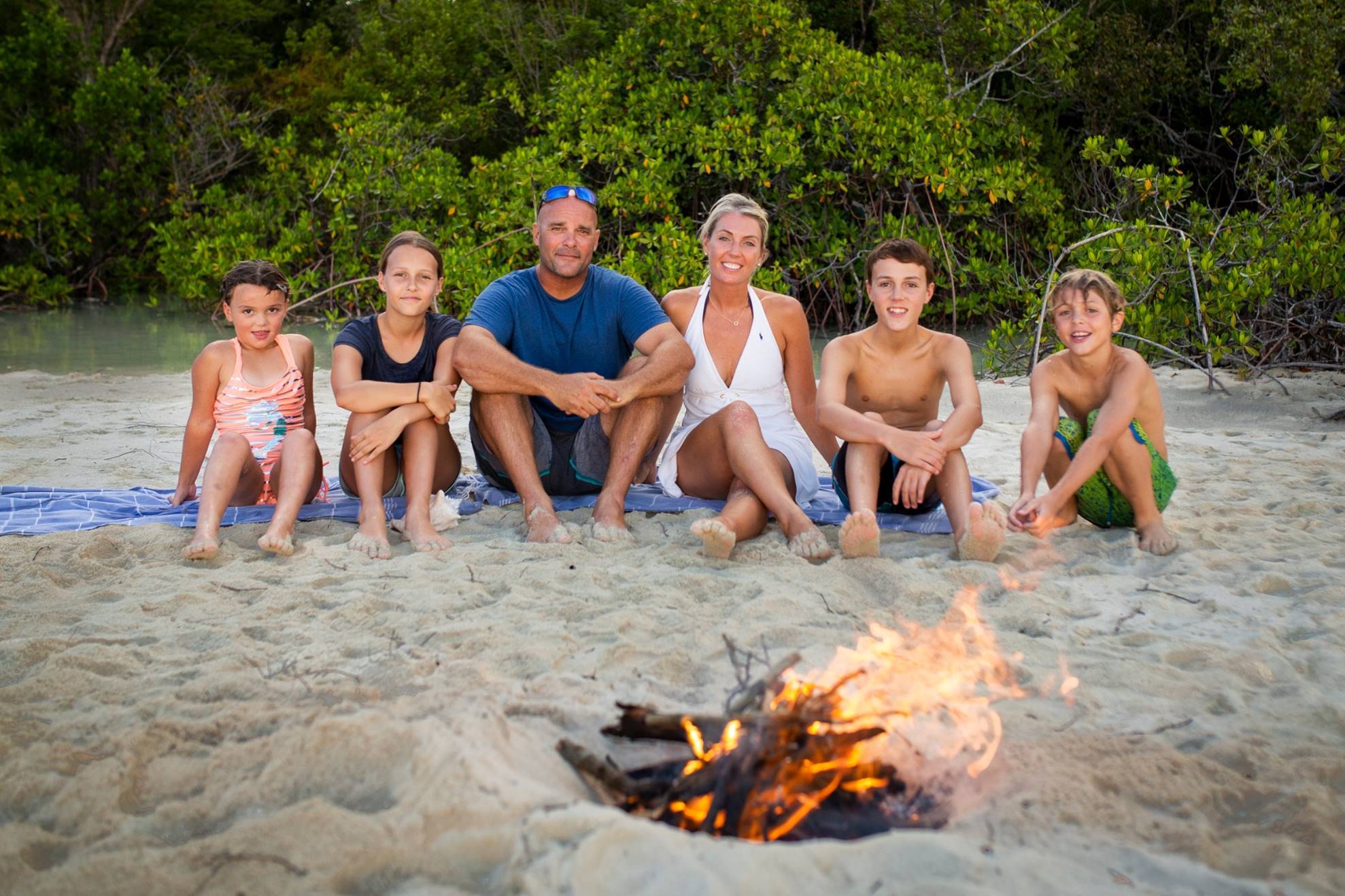 Renovation Island stars Sarah and Bryan Baeumler and their children sitting on the sand in front of a fire 