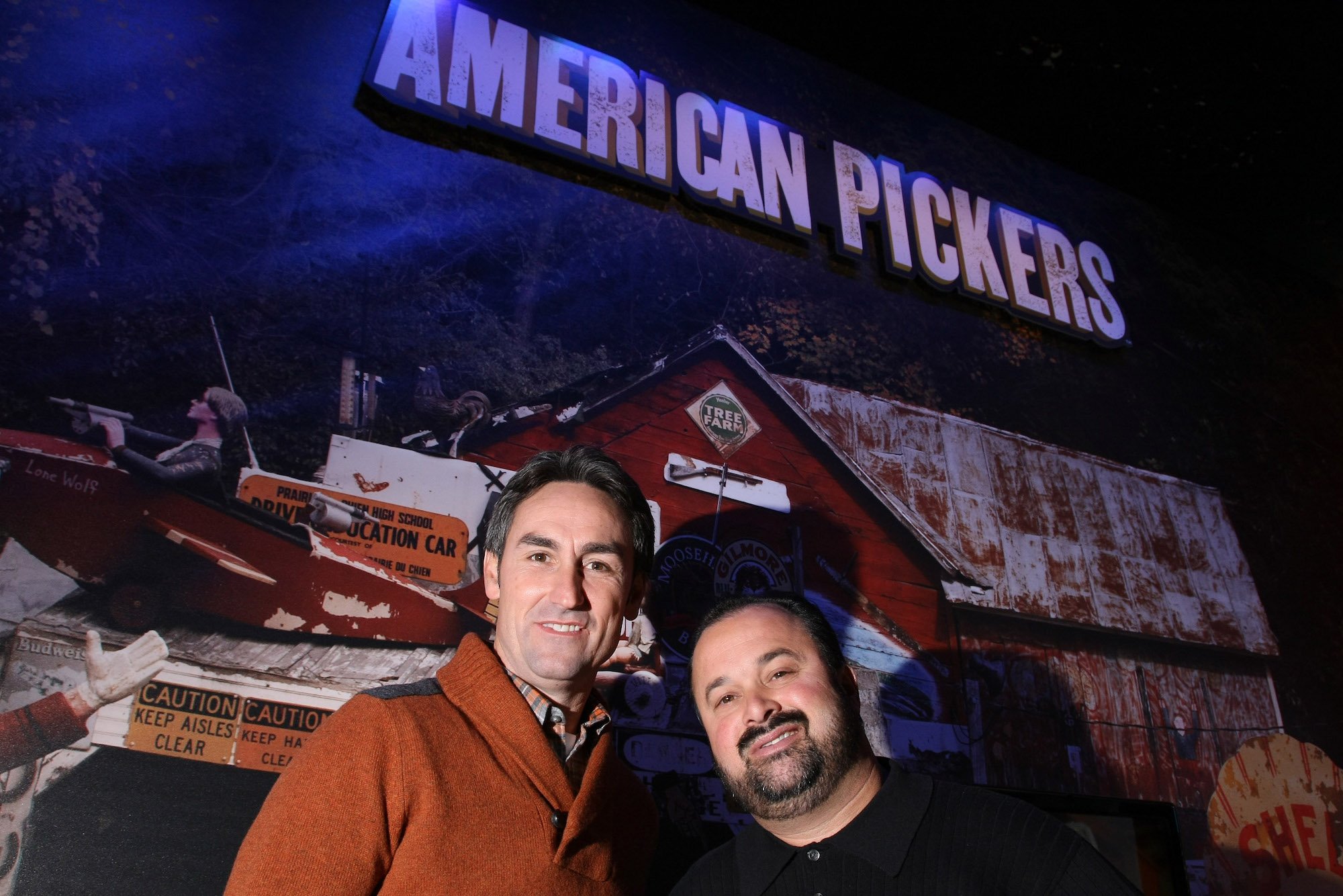 Mike Wolfe and Frank Fritz smiling in front of an American Pickers logo