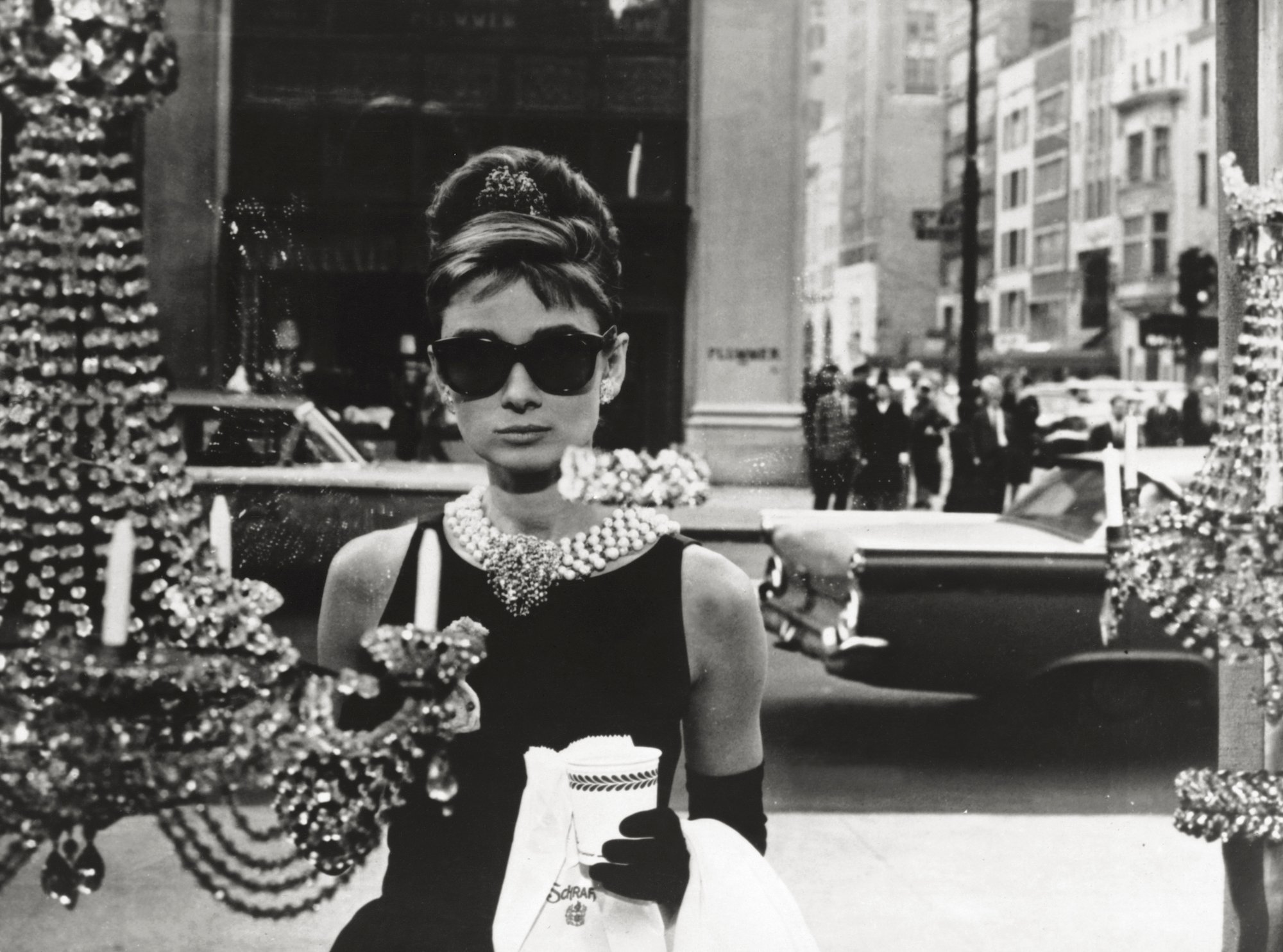 Aubrey Hepburn holding coffee and a paper bag, photographed through a window