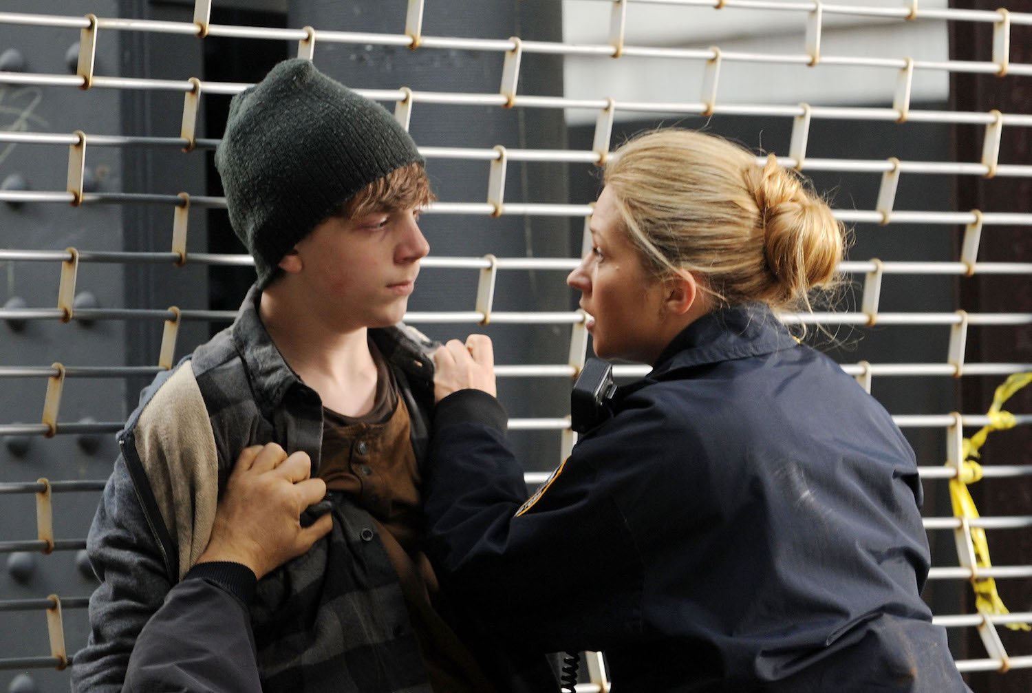 Gabriel Rush held up against a metal fence by Vanessa Ray on set of Blue Bloods