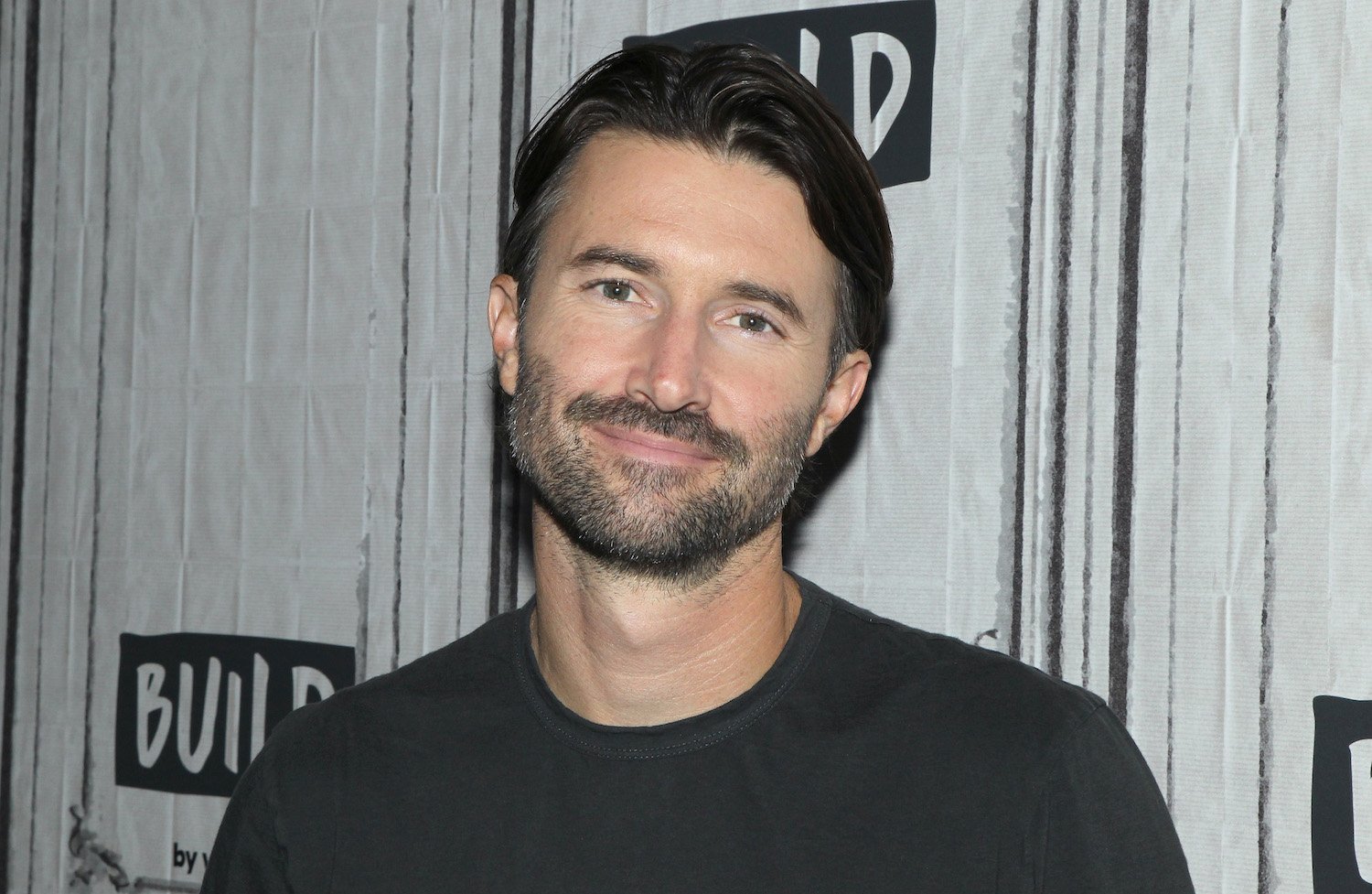 Brandon Jenner smiling at the camera in front of a white and gray background