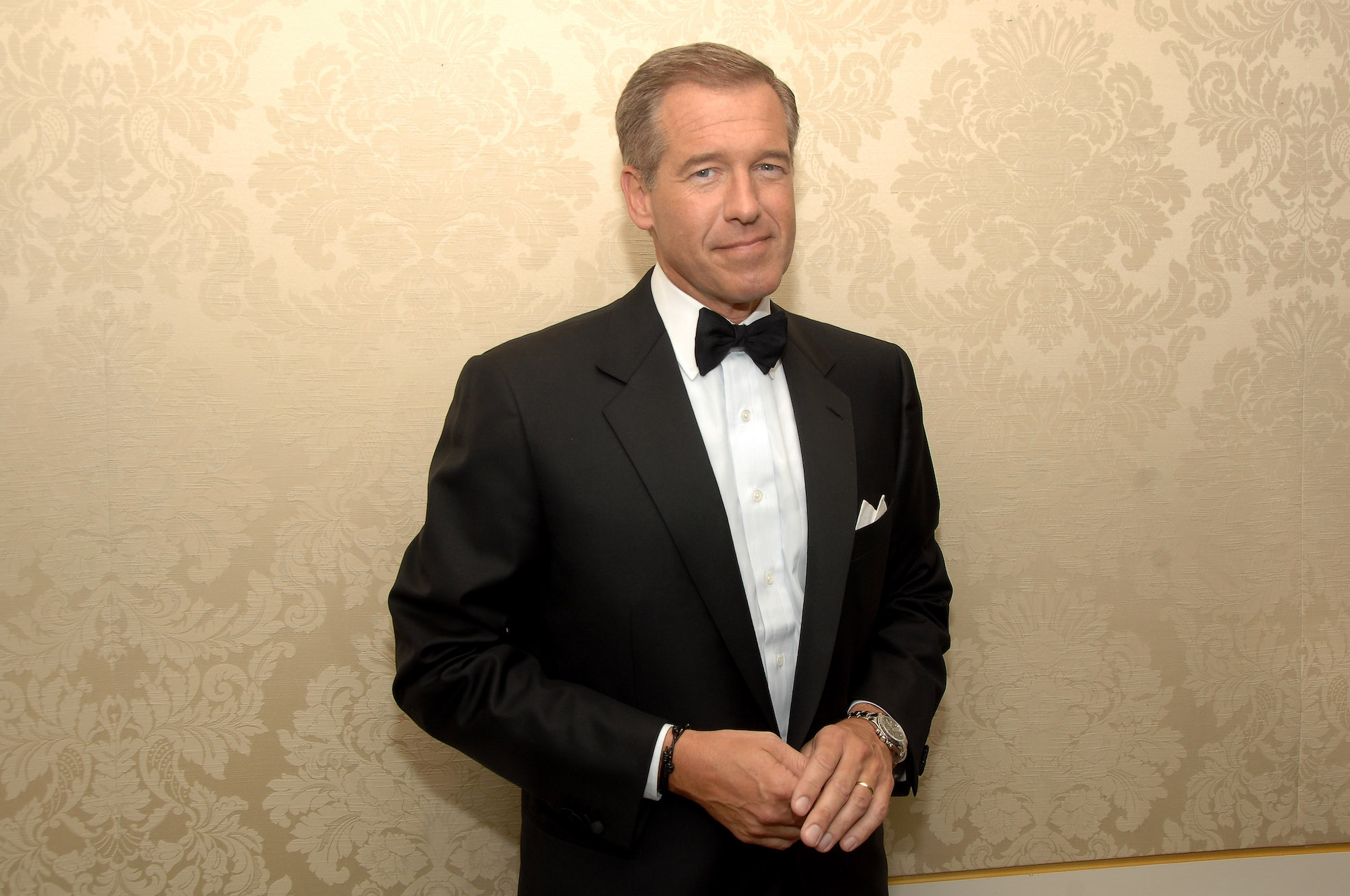 Brian Williams smiling at the camera in front of a gold wall