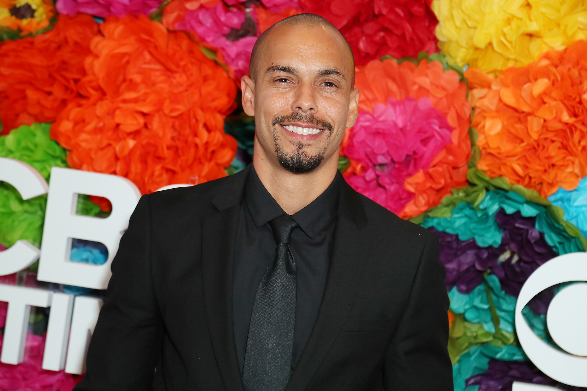 Bryton James smiling in front of a multi color floral background