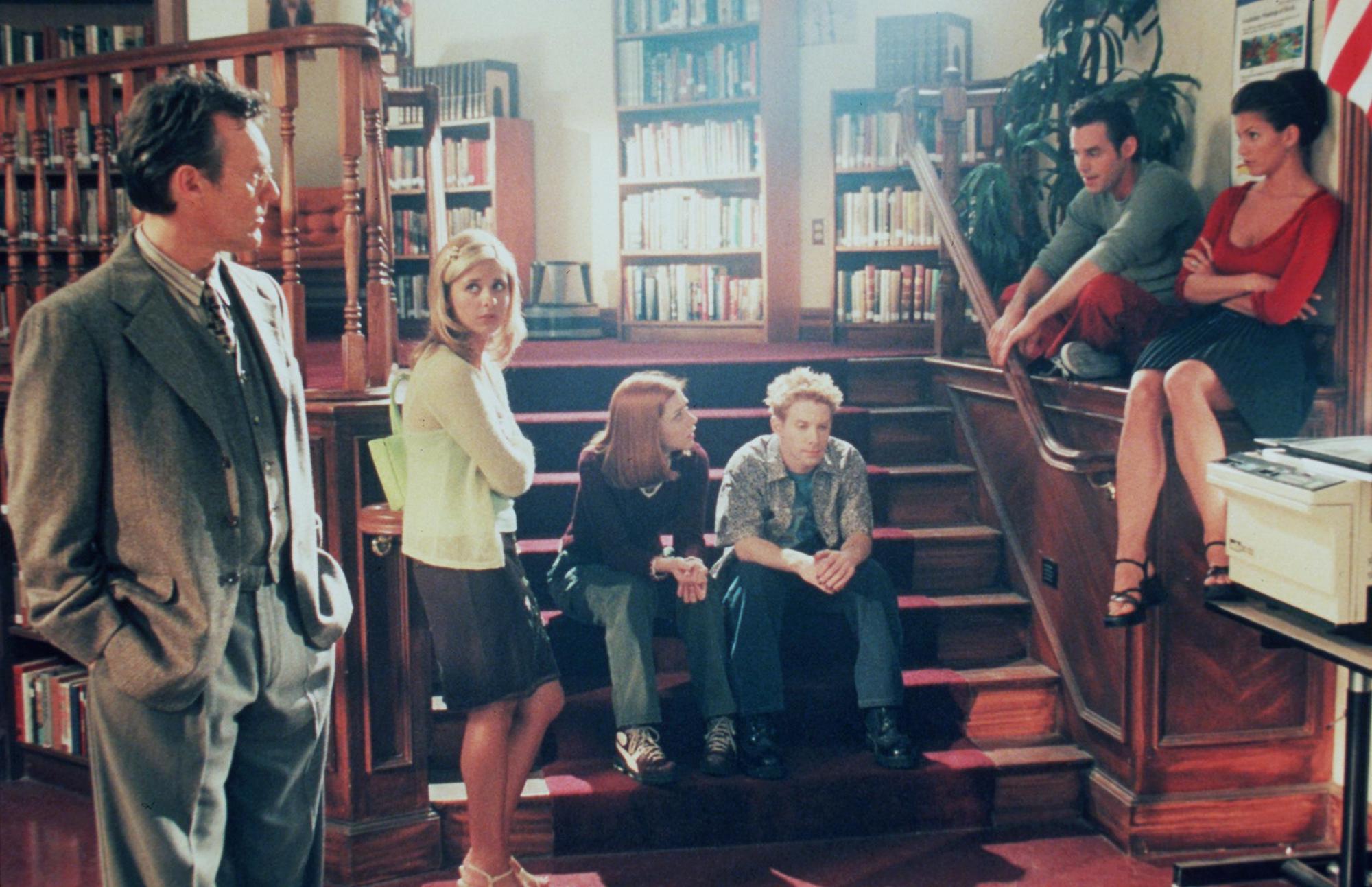 l-r: Anthony Stewart Head, Sarah Michelle Gellar, Alyson Hannigan, Seth Green, Nicholas Brendon and Charisma Carpenter sitting around a library on 'Buffy the Vampire Slayer'