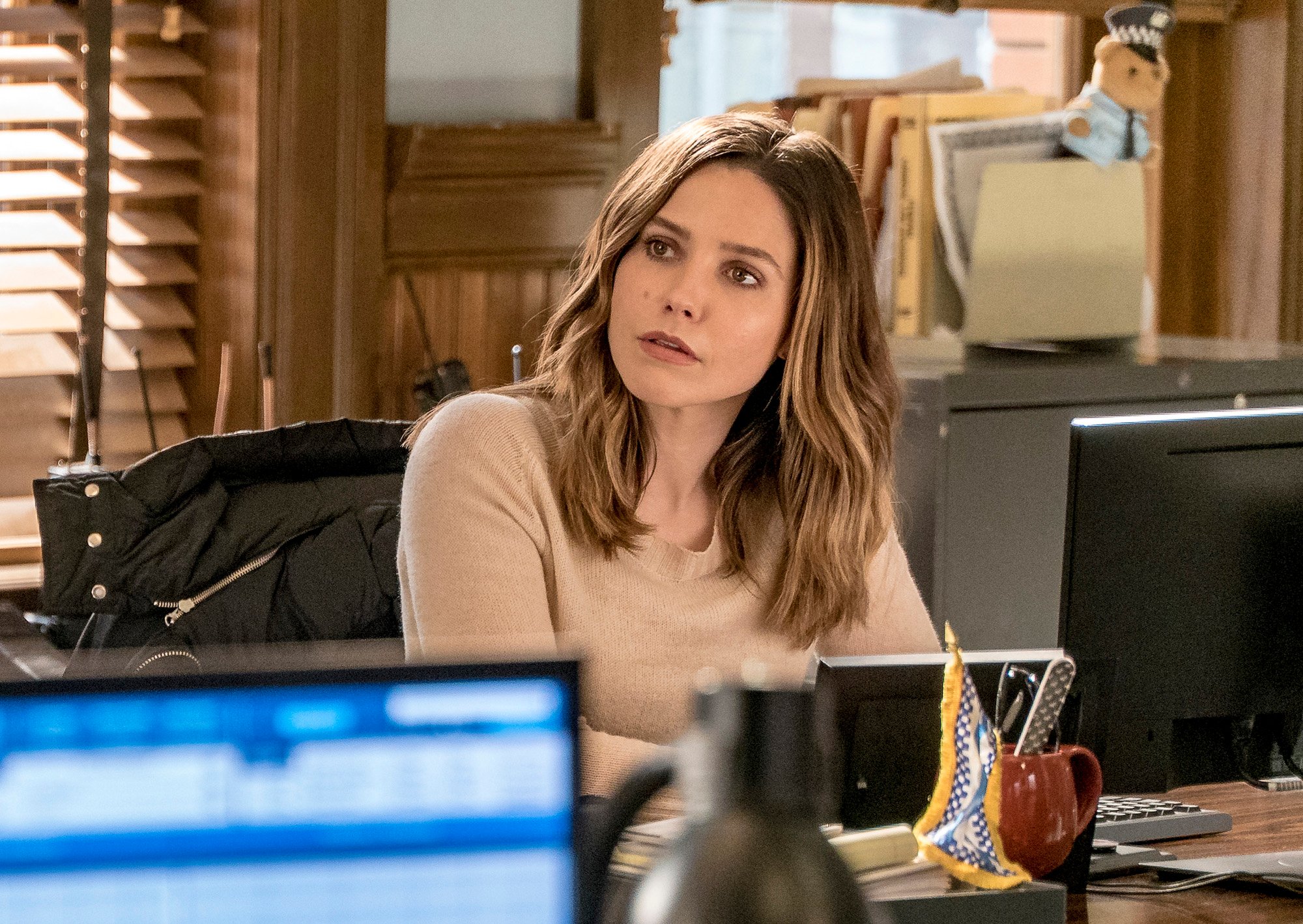 Sophia Bush as Erin Lindsay sitting at a desk, looking to the side