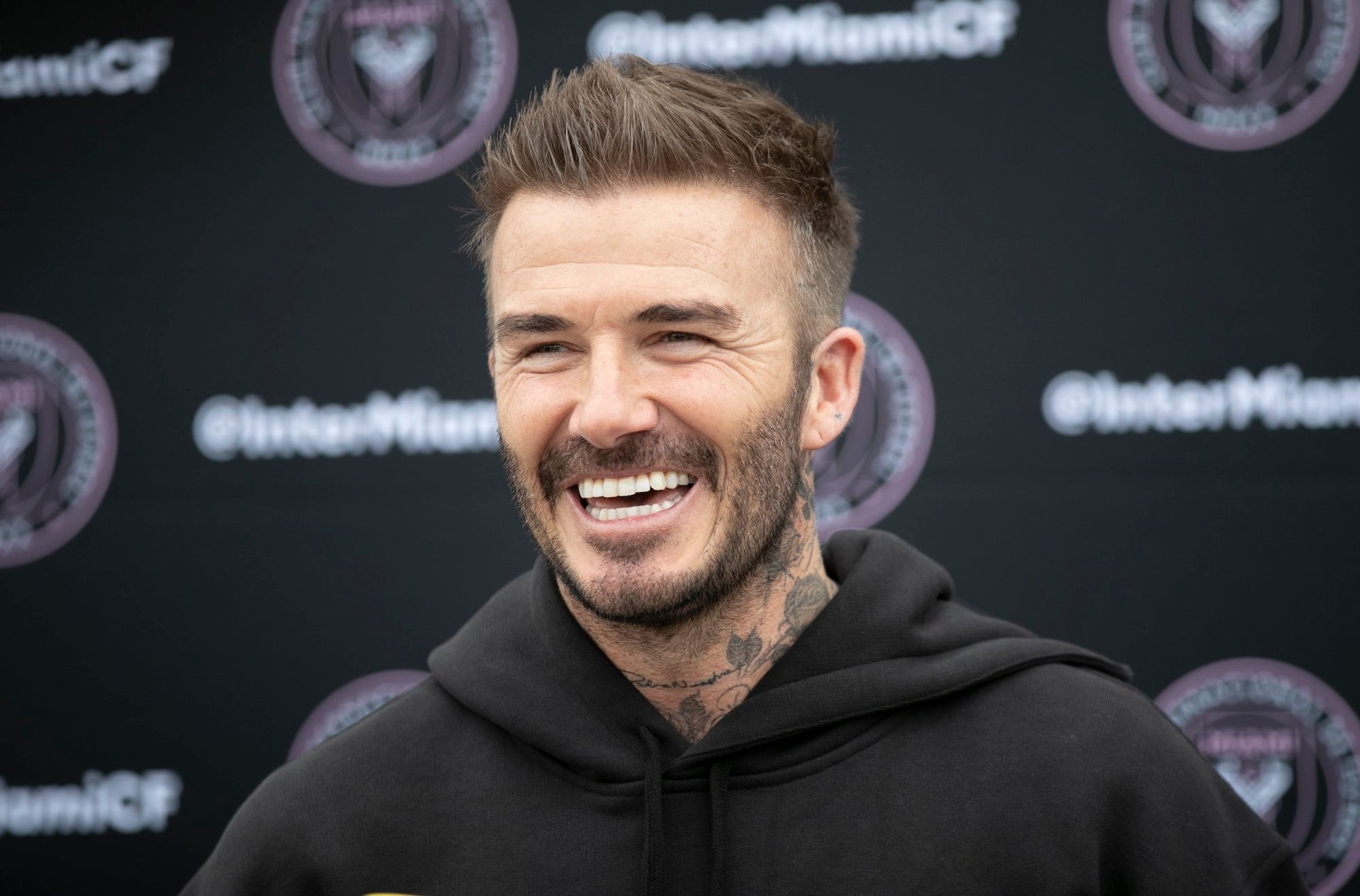 David Beckham laughing in front of a blurry black background