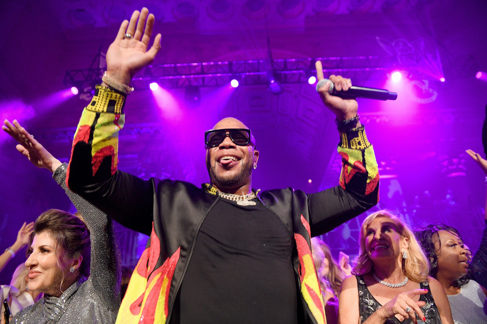 Flo Rida smiling with his hands up holding a mic