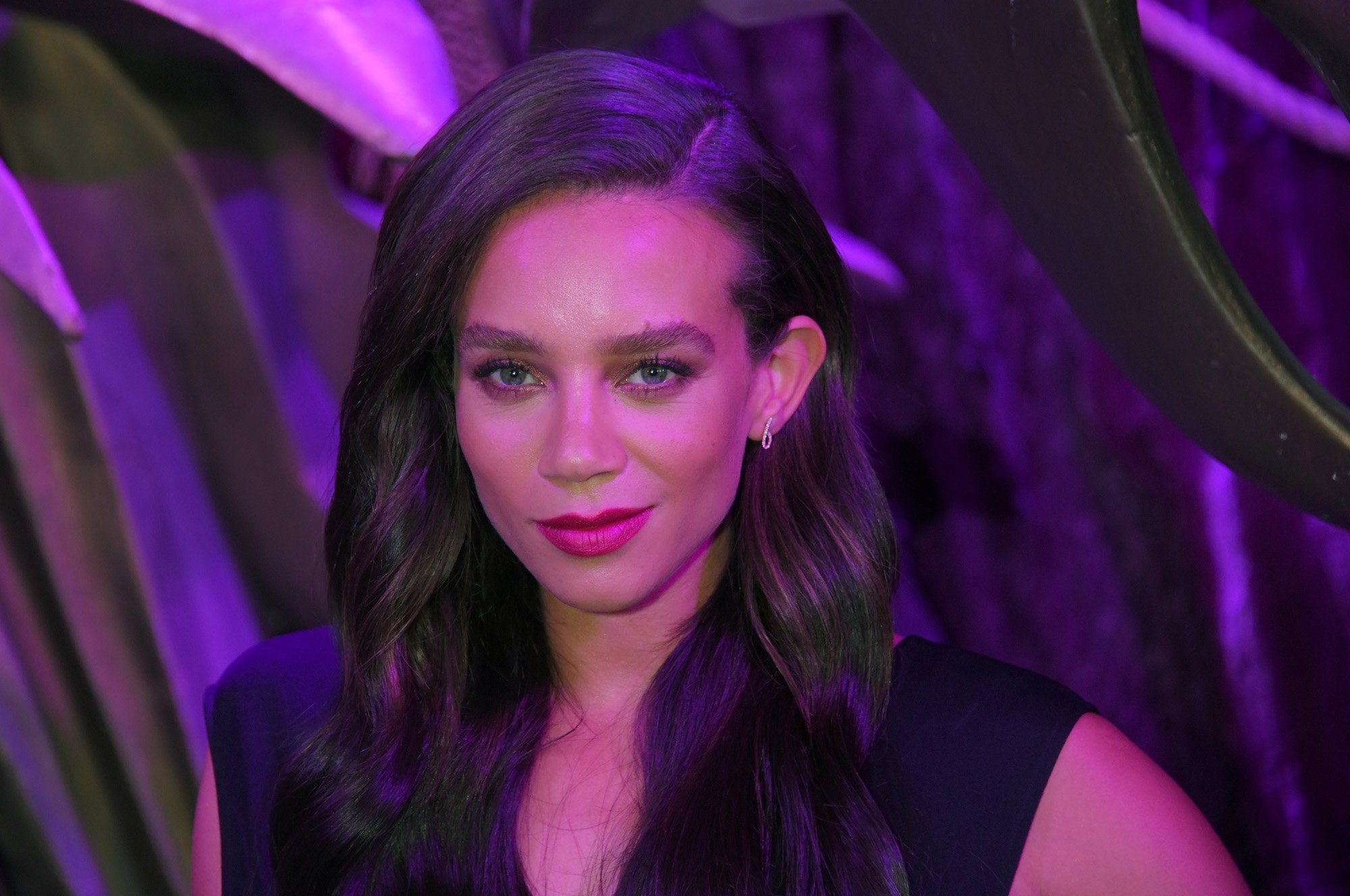 Hannah John-Kamen smiling in front of a purple background