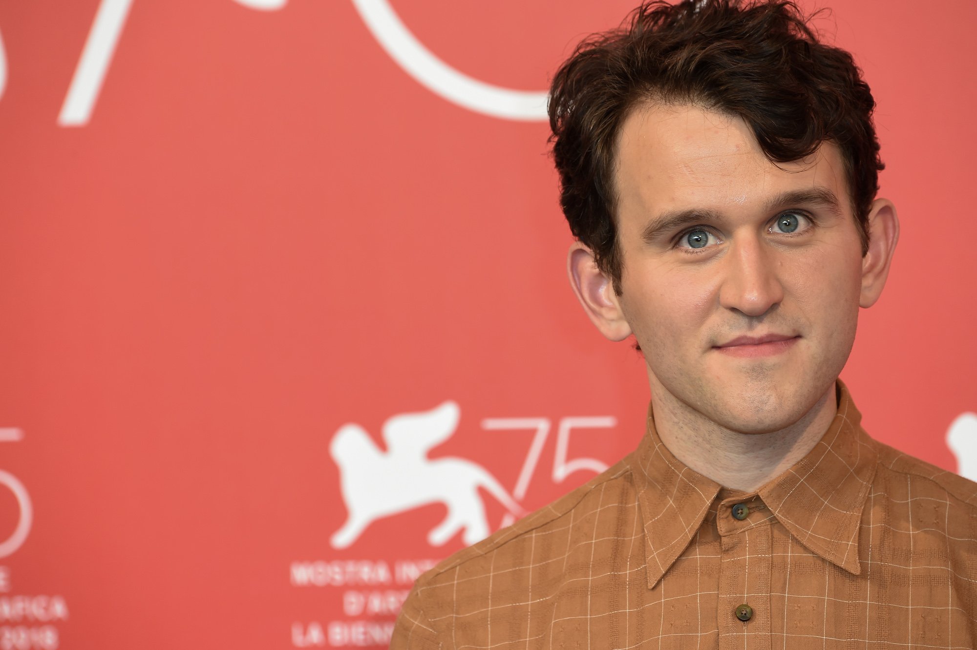 Harry Melling smiling at the camera in front of a pink background