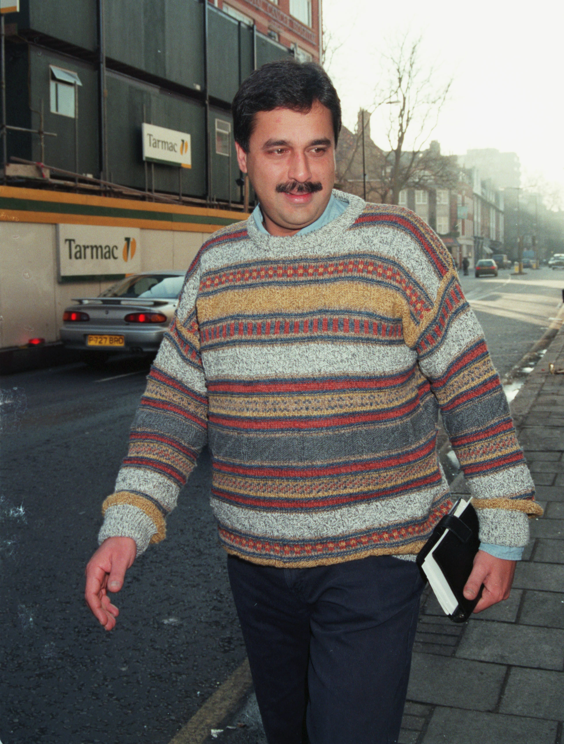 Hasnat Khan in a multicolored striped sweater, holding a book