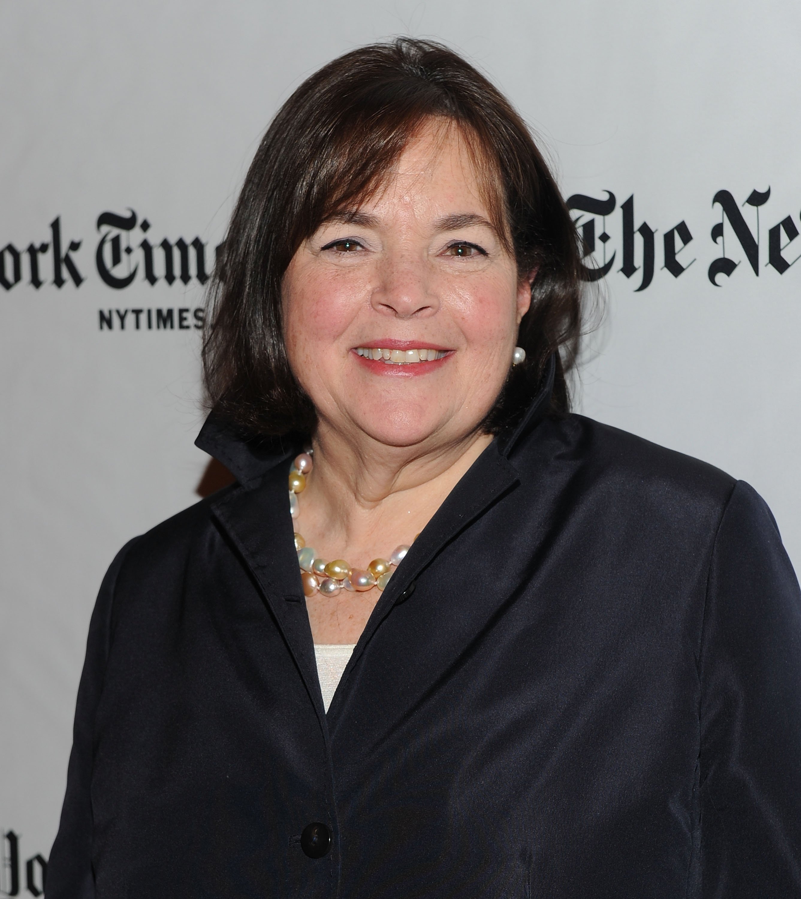 Ina Garten smiles wearing a black blazer in front of a white background