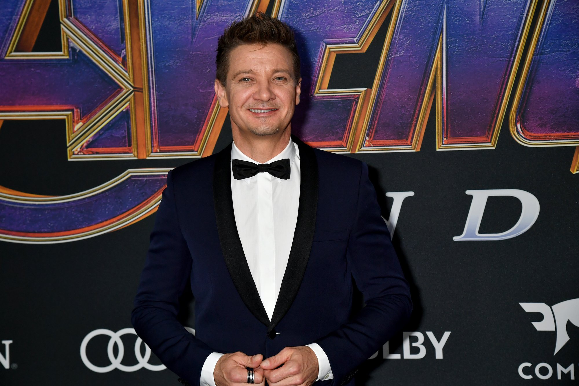 Jeremy Renner smiling wearing a suit and bow tie