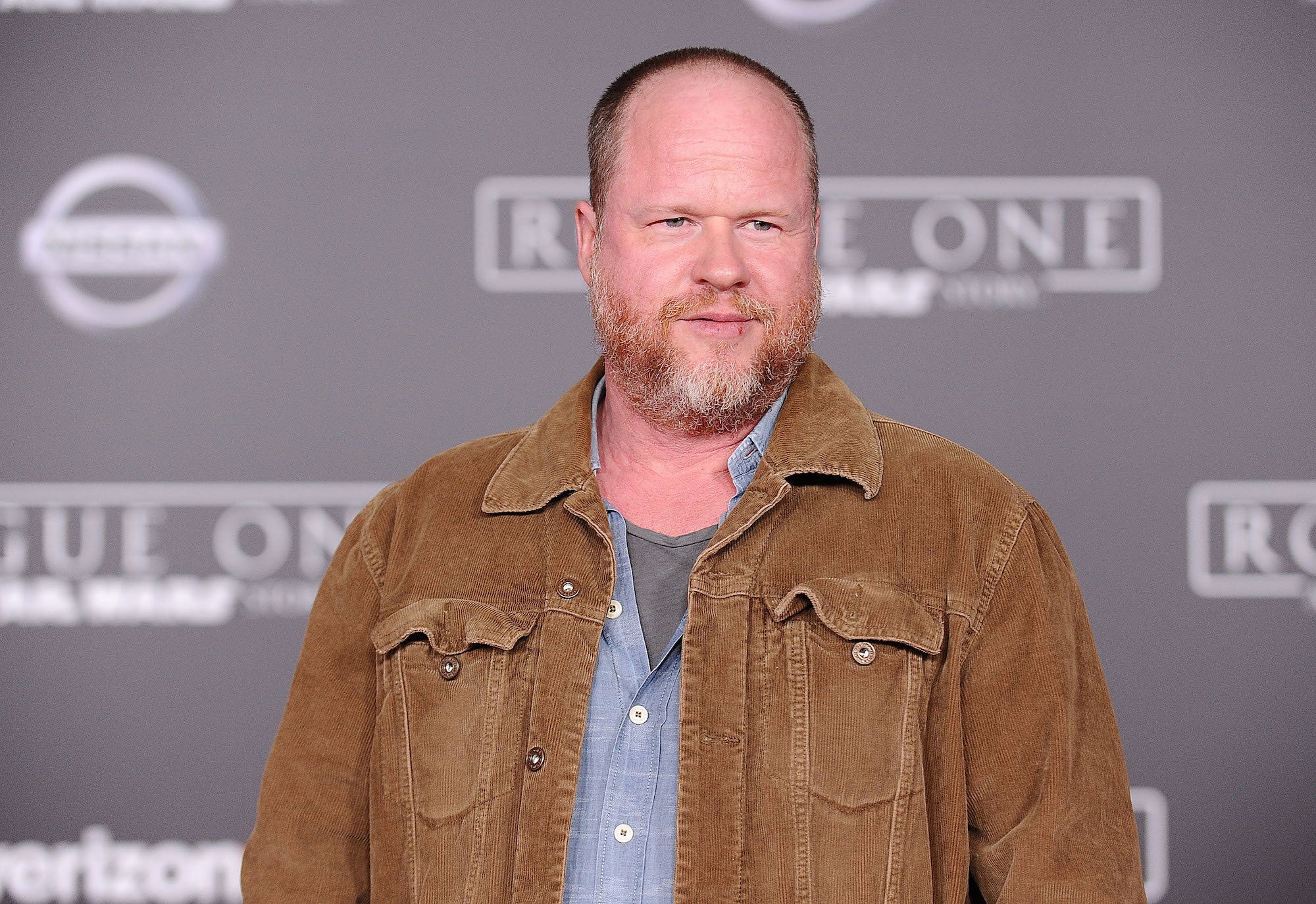 Joss Whedon looking away from the camera in front of a gray background