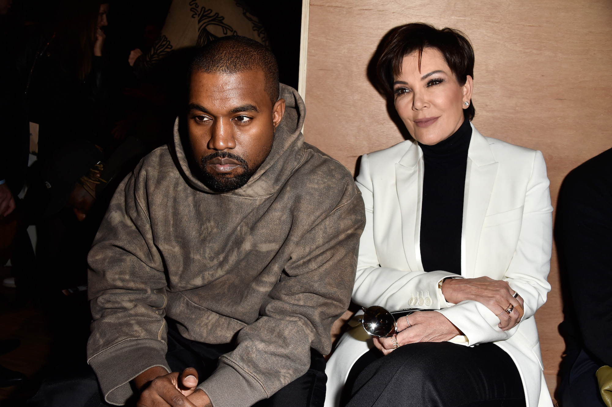 Kanye West looking off camera leaning forward next to Kris Jenner