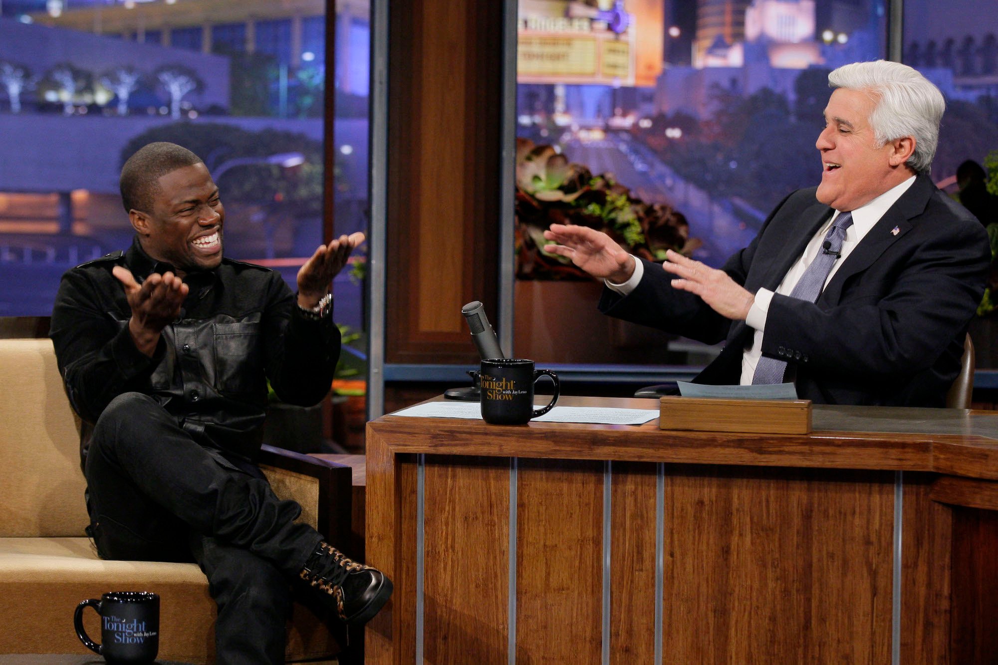 Kevin Hart and Jay Leno laughing, both with their hands raise