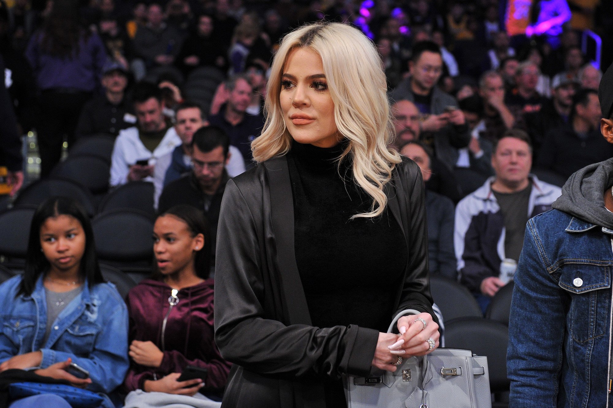 Khloé Kardashian slightly smiling on a basketball court, looking off camera