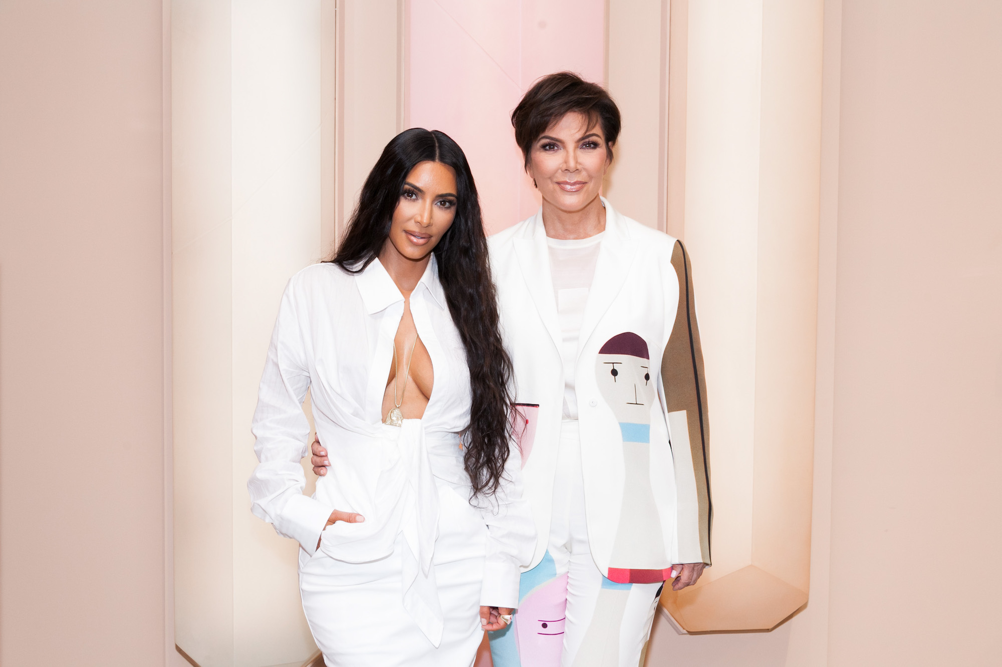 Kim Kardashian West and Kris Jenner smiling in front of a light pink background