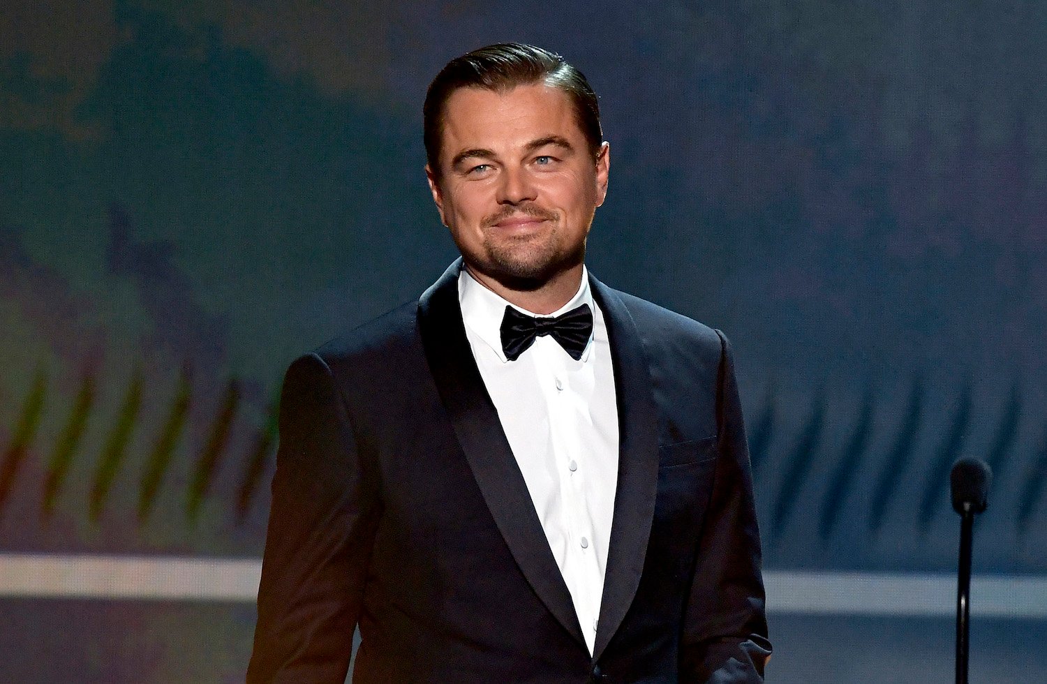 Leonardo DiCaprio smiling, looking off camera, wearing a tux