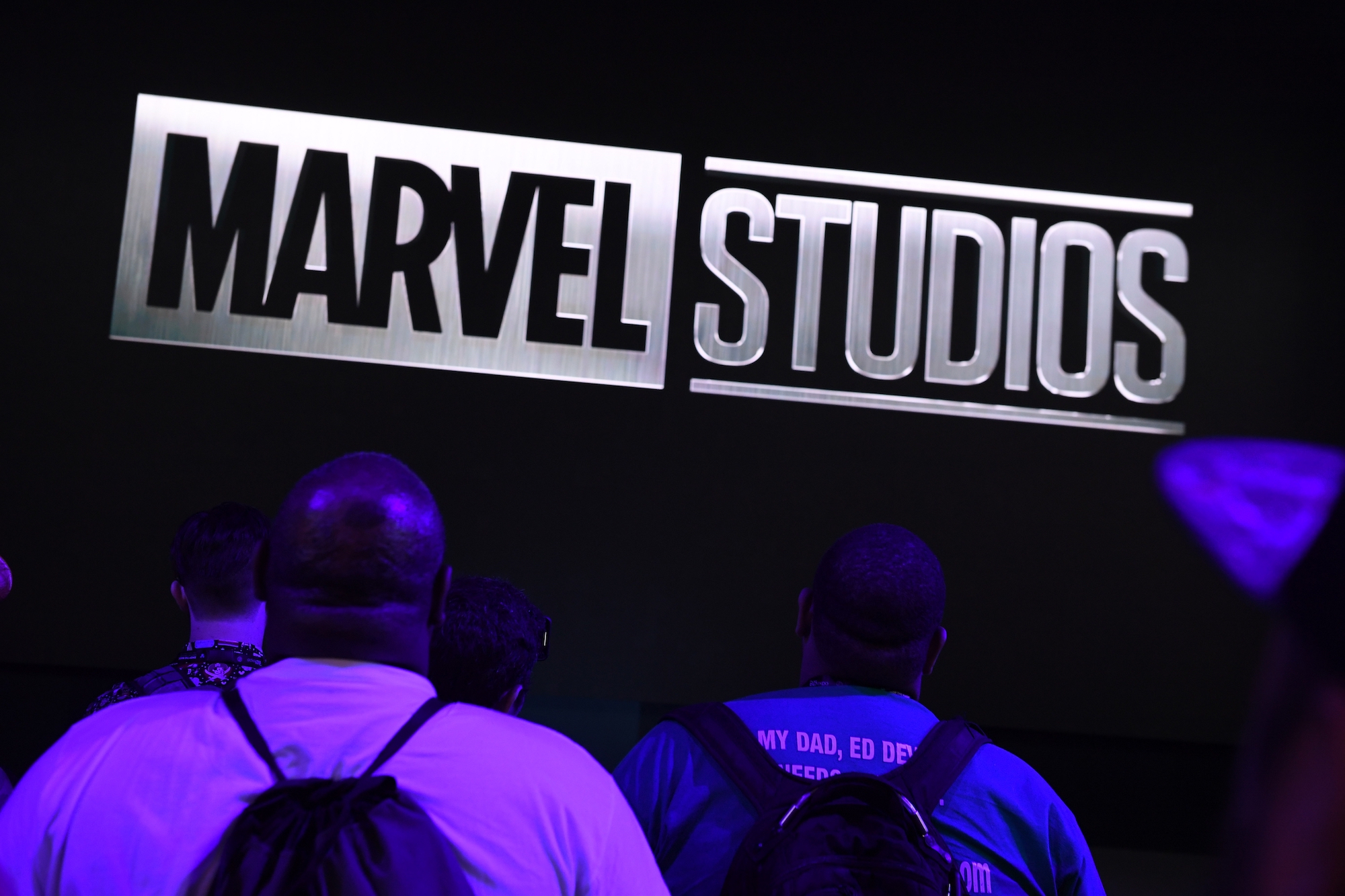Marvel Studios logo lit up with people in backpacks looking up at the logo