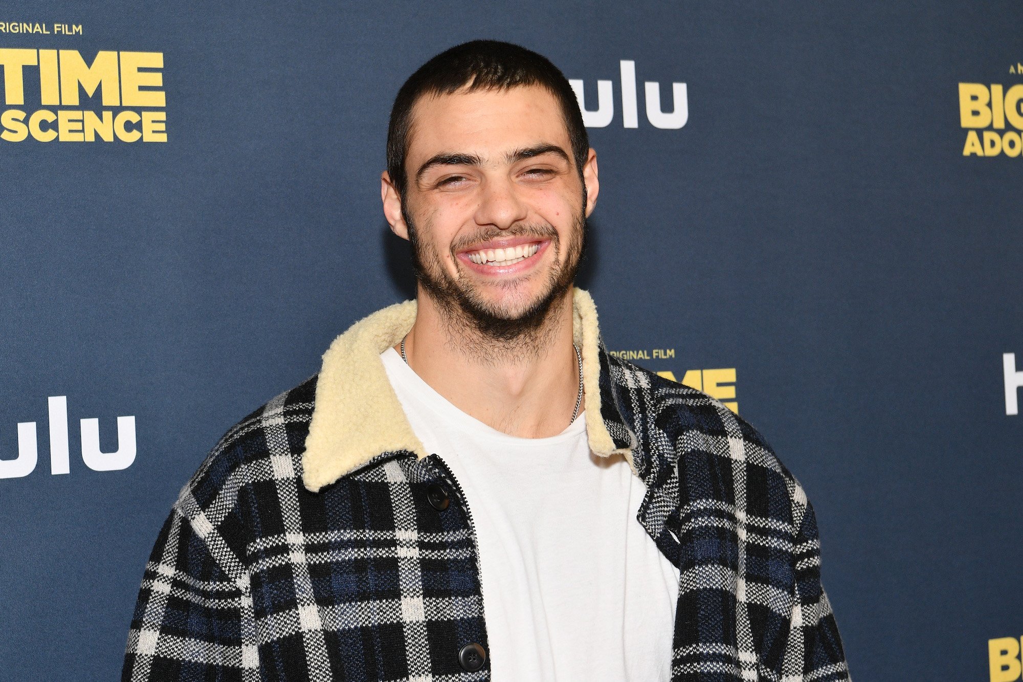 Noah Centineo smiling in front of a navy blue background